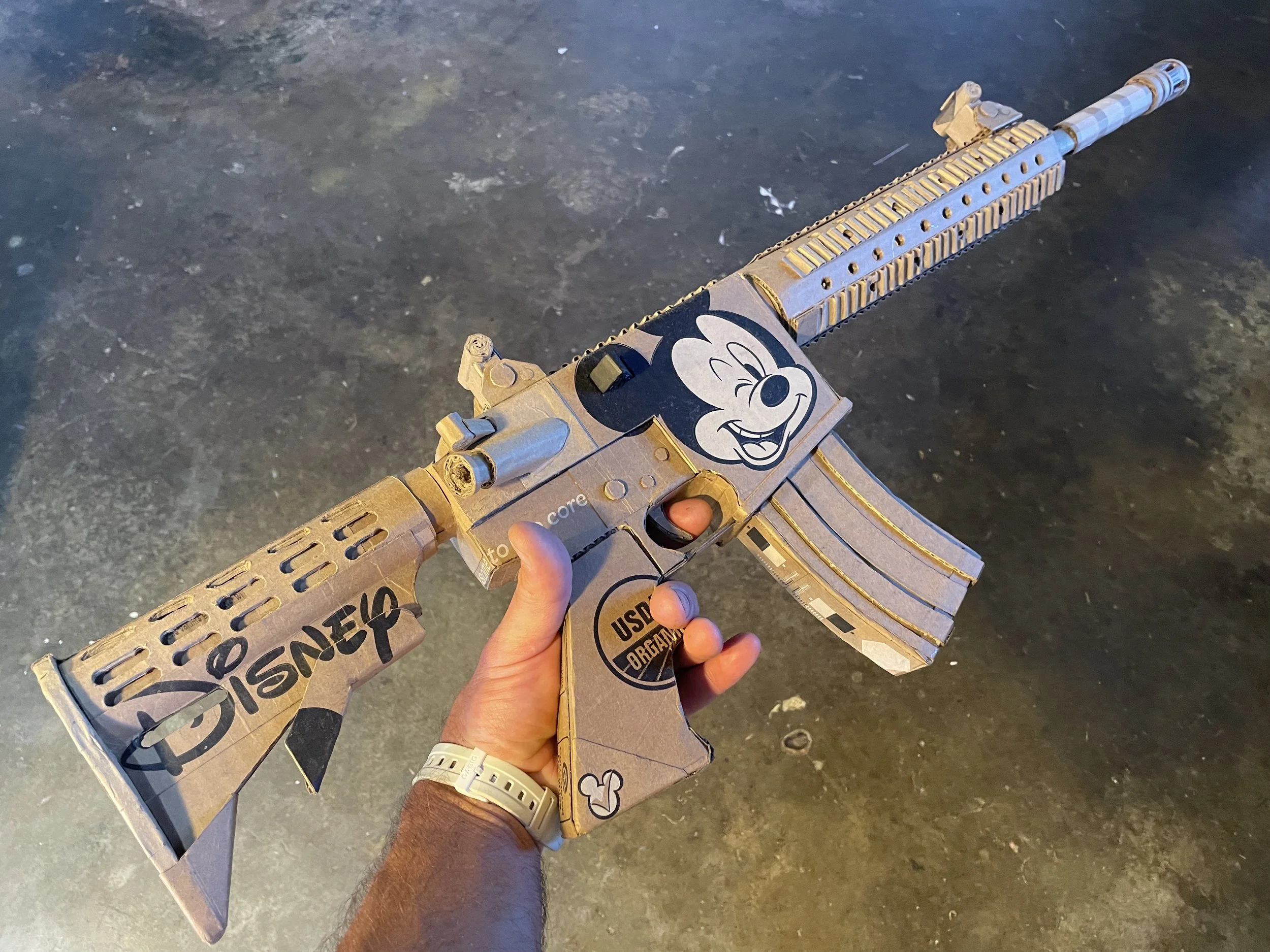 Disney Mickey Mouse anti-capitalist corporate satire Florida mass shooting cardboard recycled material art sculpture political action parody