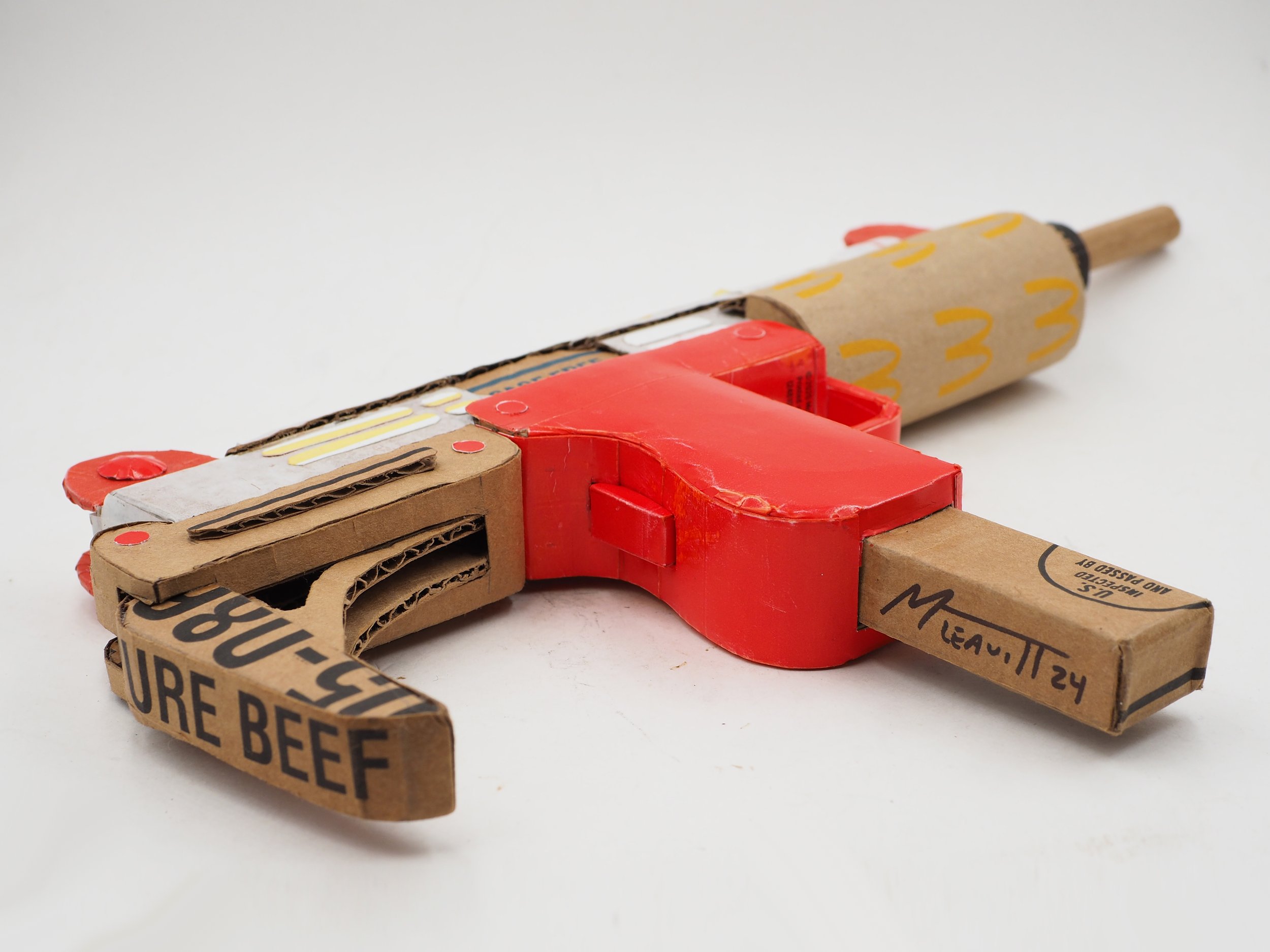 Mass shooting cardboard Uzi recycled material art sculpture political action McDonalds corporate culture parody
