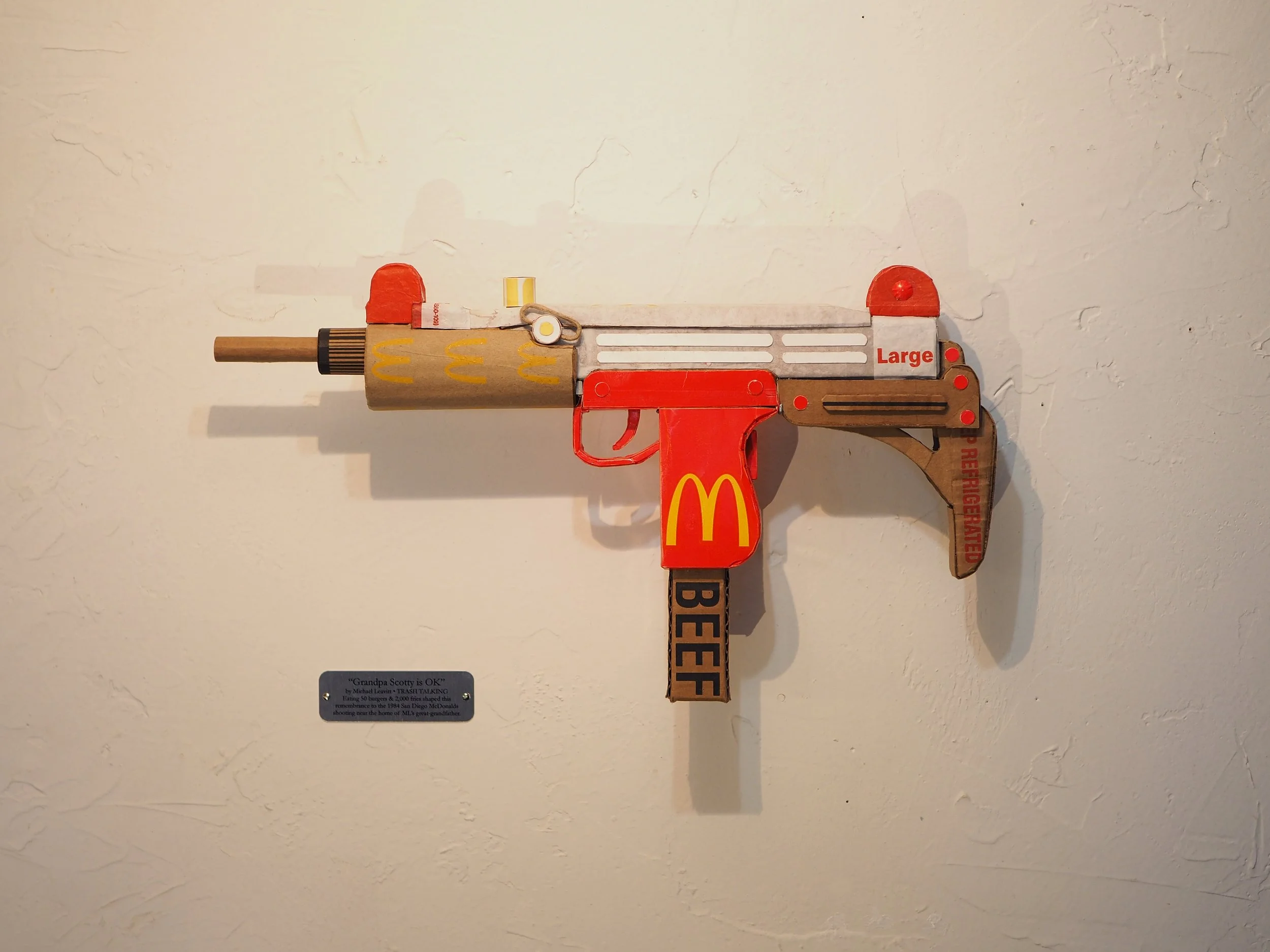 Mass shooting cardboard Uzi recycled material art sculpture political action McDonalds corporate culture parody