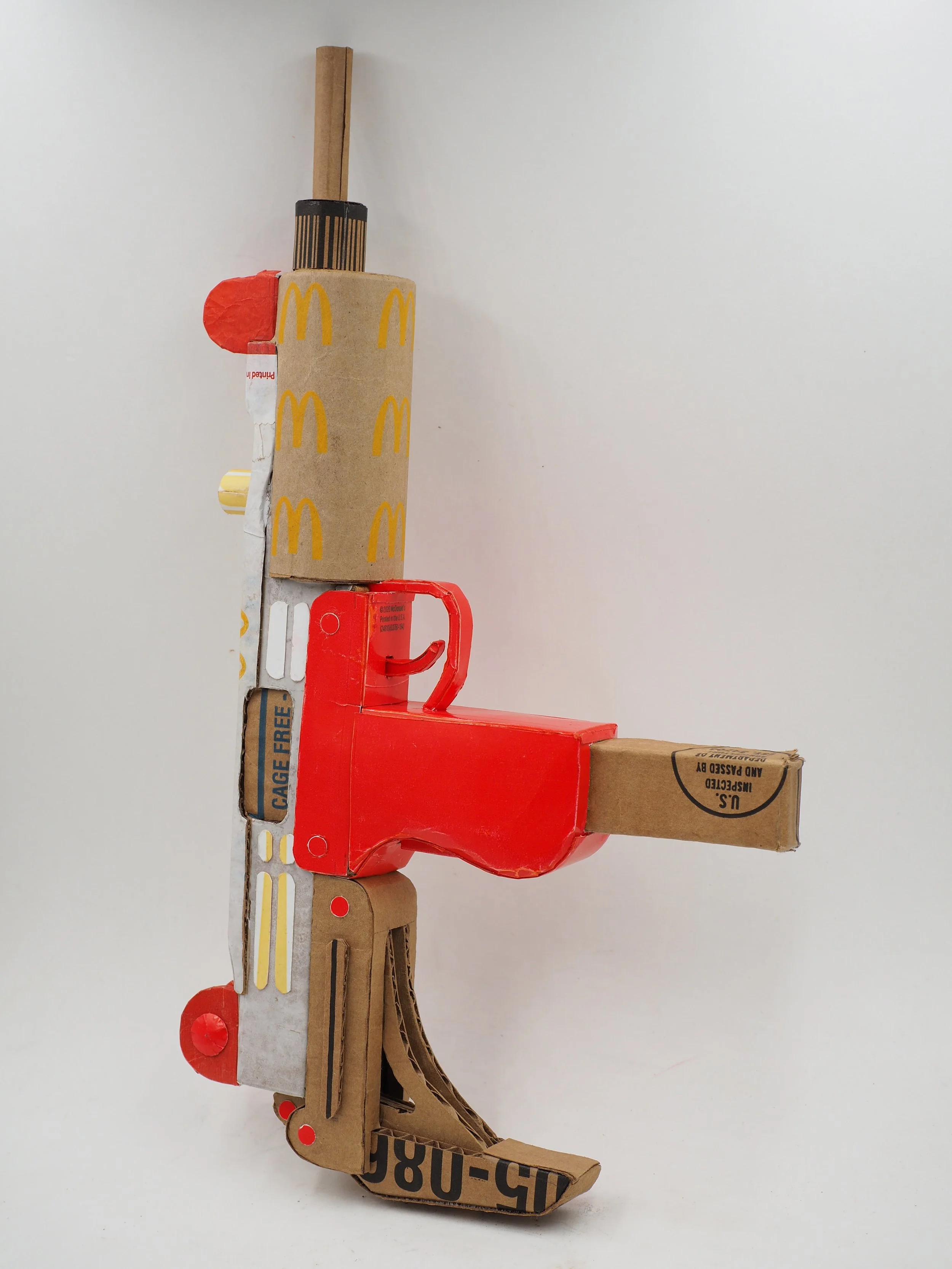 Mass shooting cardboard Uzi recycled material art sculpture political action McDonalds corporate culture parody