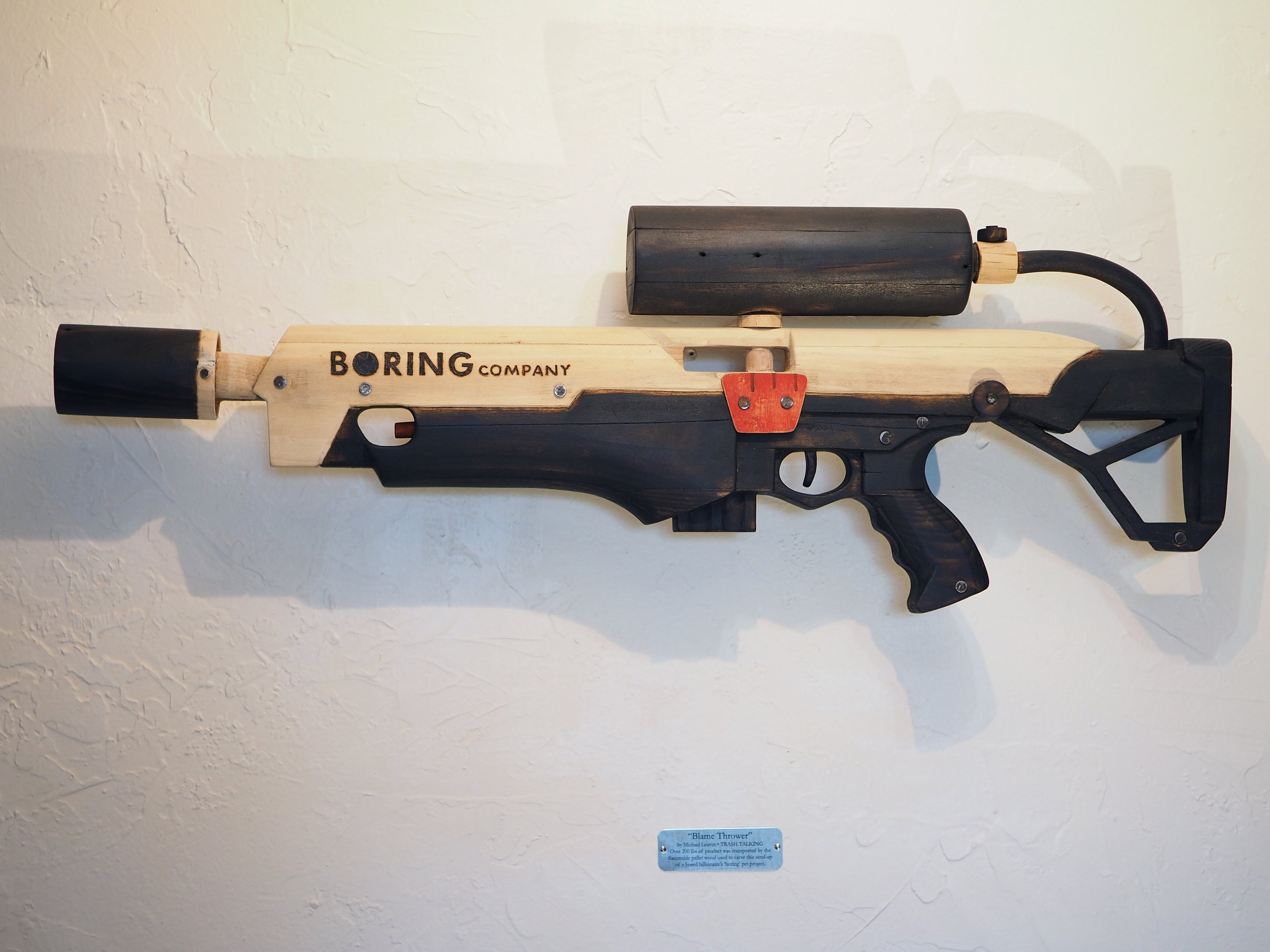 Elon Musk Boring Company flame thrower Twitter X Tesla corporate culture anti-capitalist woodworking wood sculpture recycled reclaimed pallet wood satire celebrity parody art