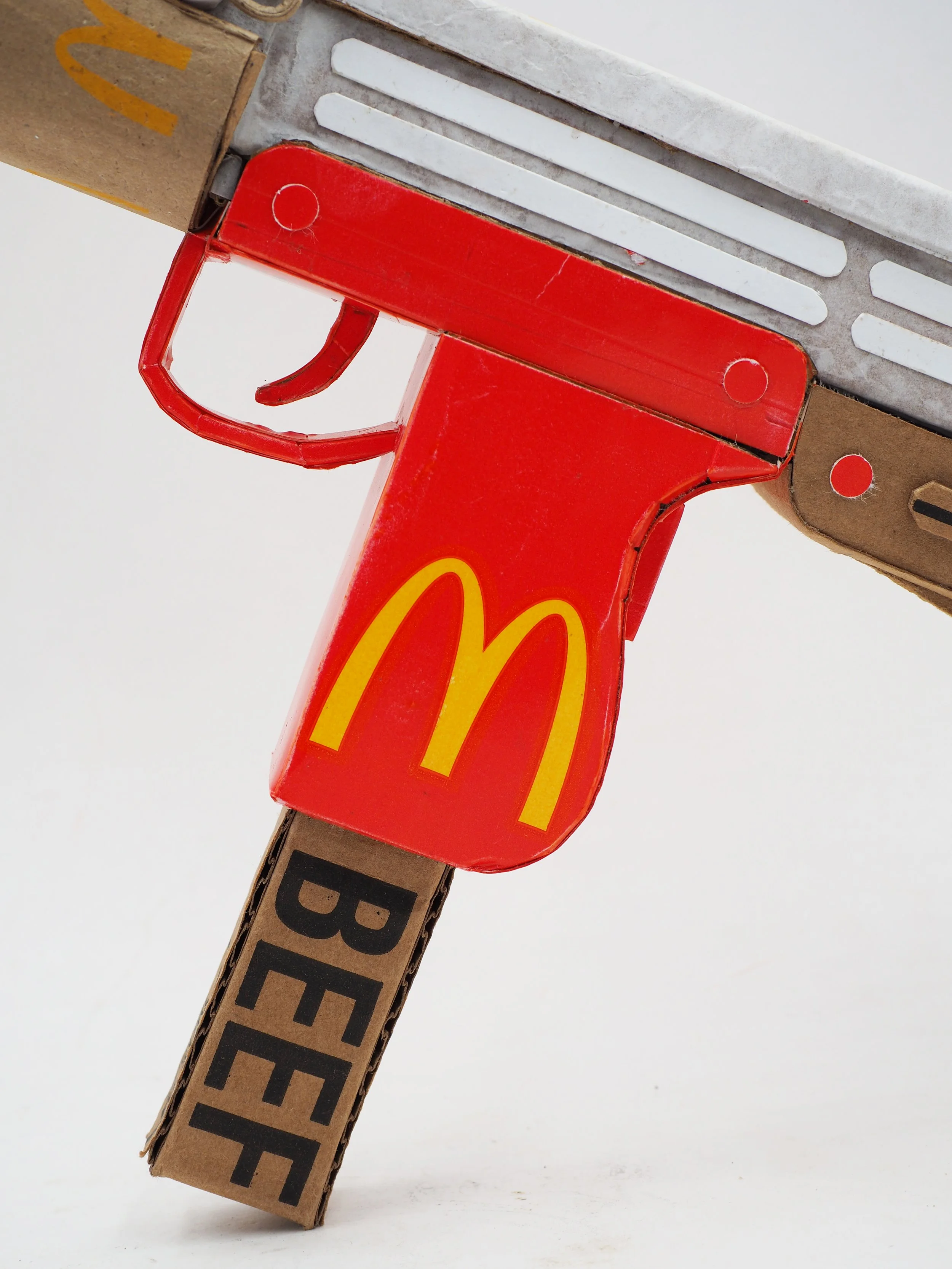 Mass shooting cardboard Uzi recycled material art sculpture political action McDonalds corporate culture parody