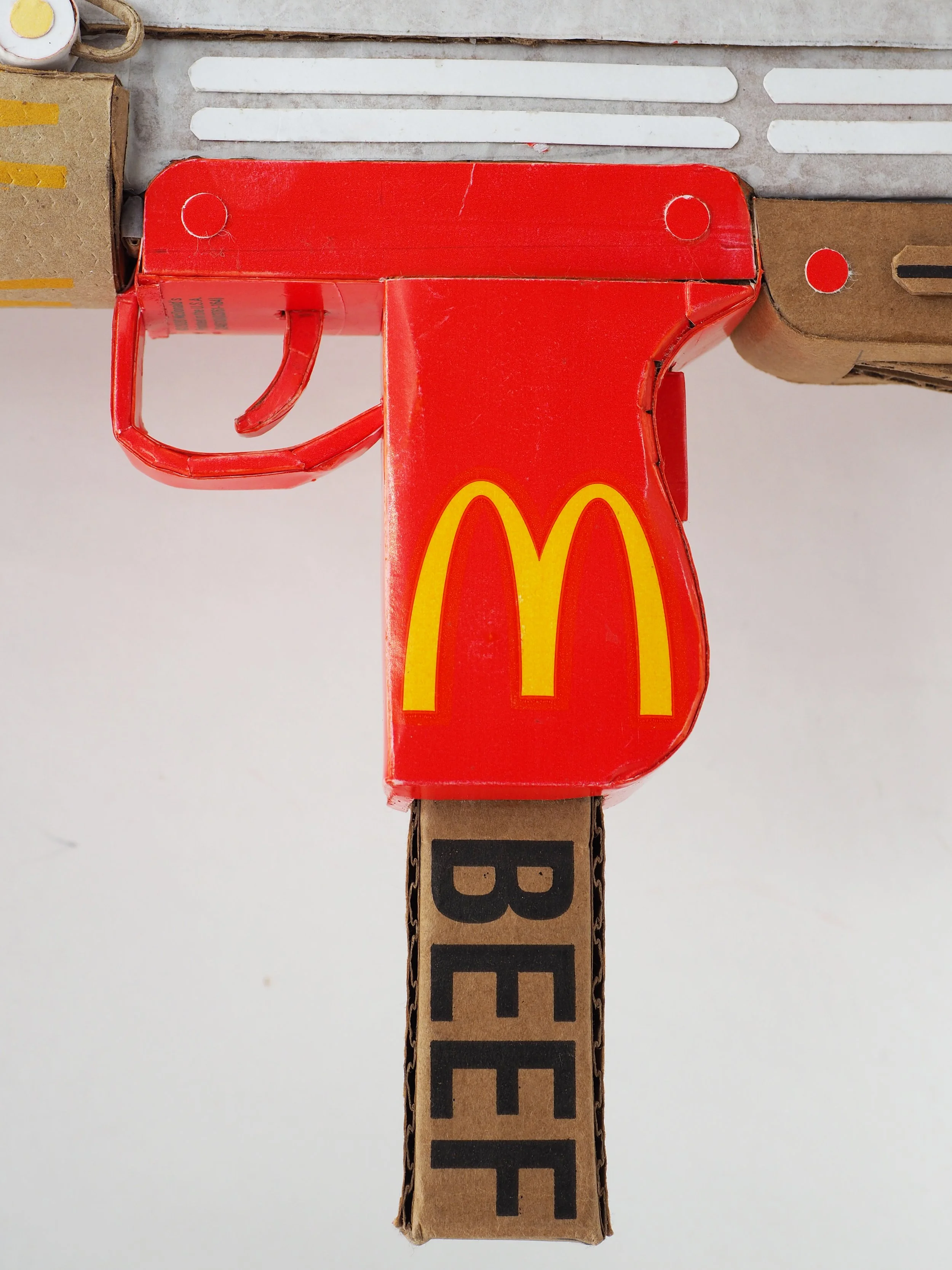 Mass shooting cardboard Uzi recycled material art sculpture political action McDonalds corporate culture parody