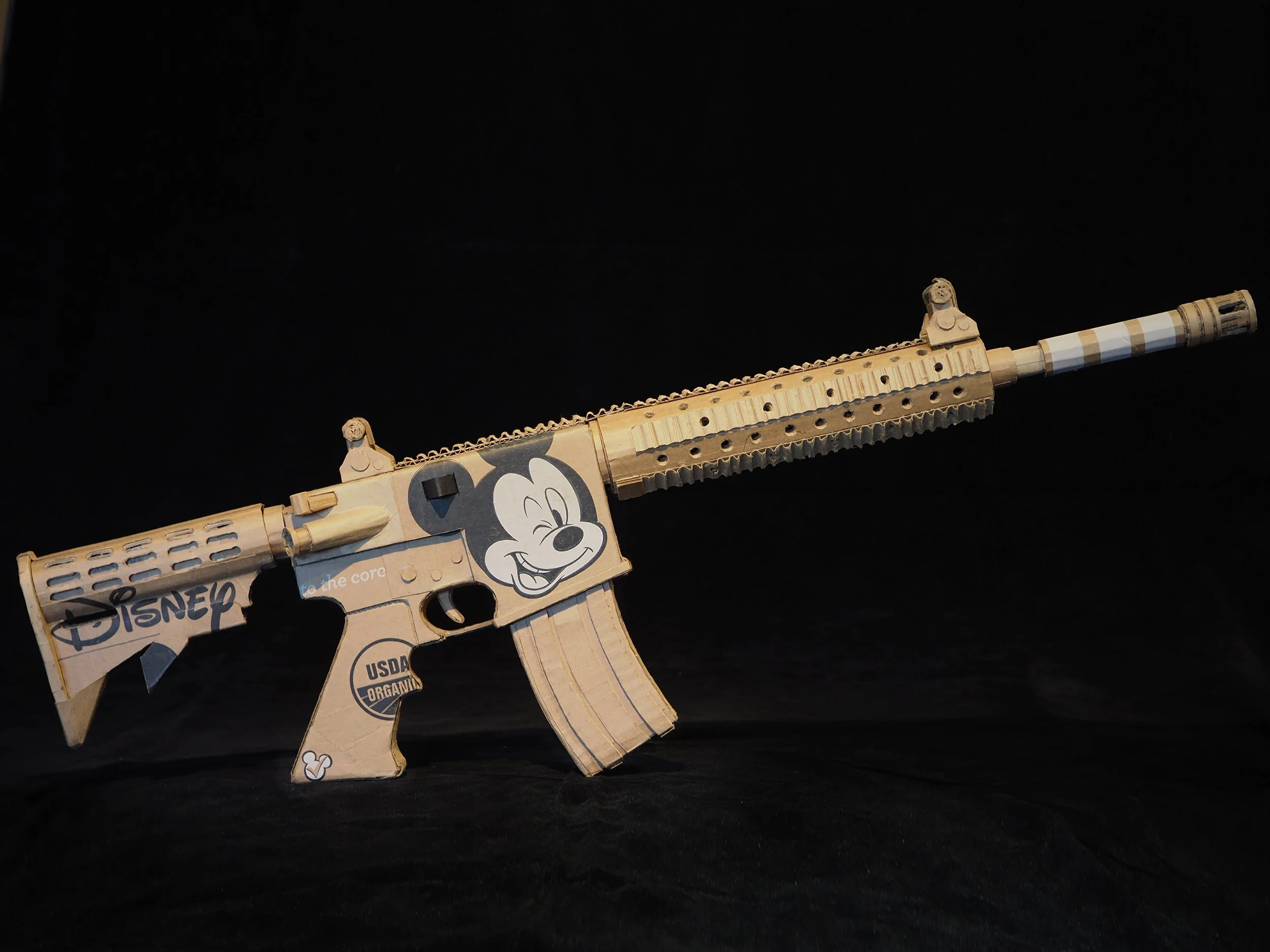 Disney Mickey Mouse anti-capitalist satire Florida mass shooting cardboard recycled material art sculpture political action parody