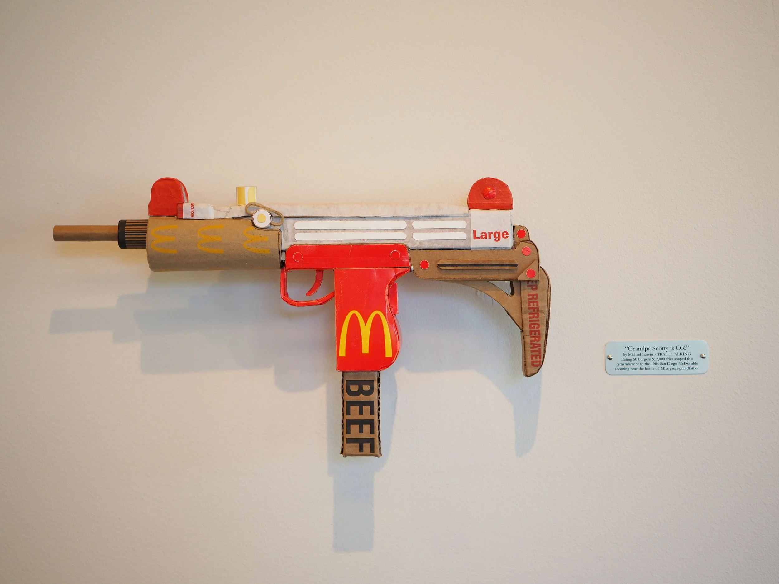 Mass shooting cardboard Uzi recycled material art sculpture political action McDonalds corporate culture parody