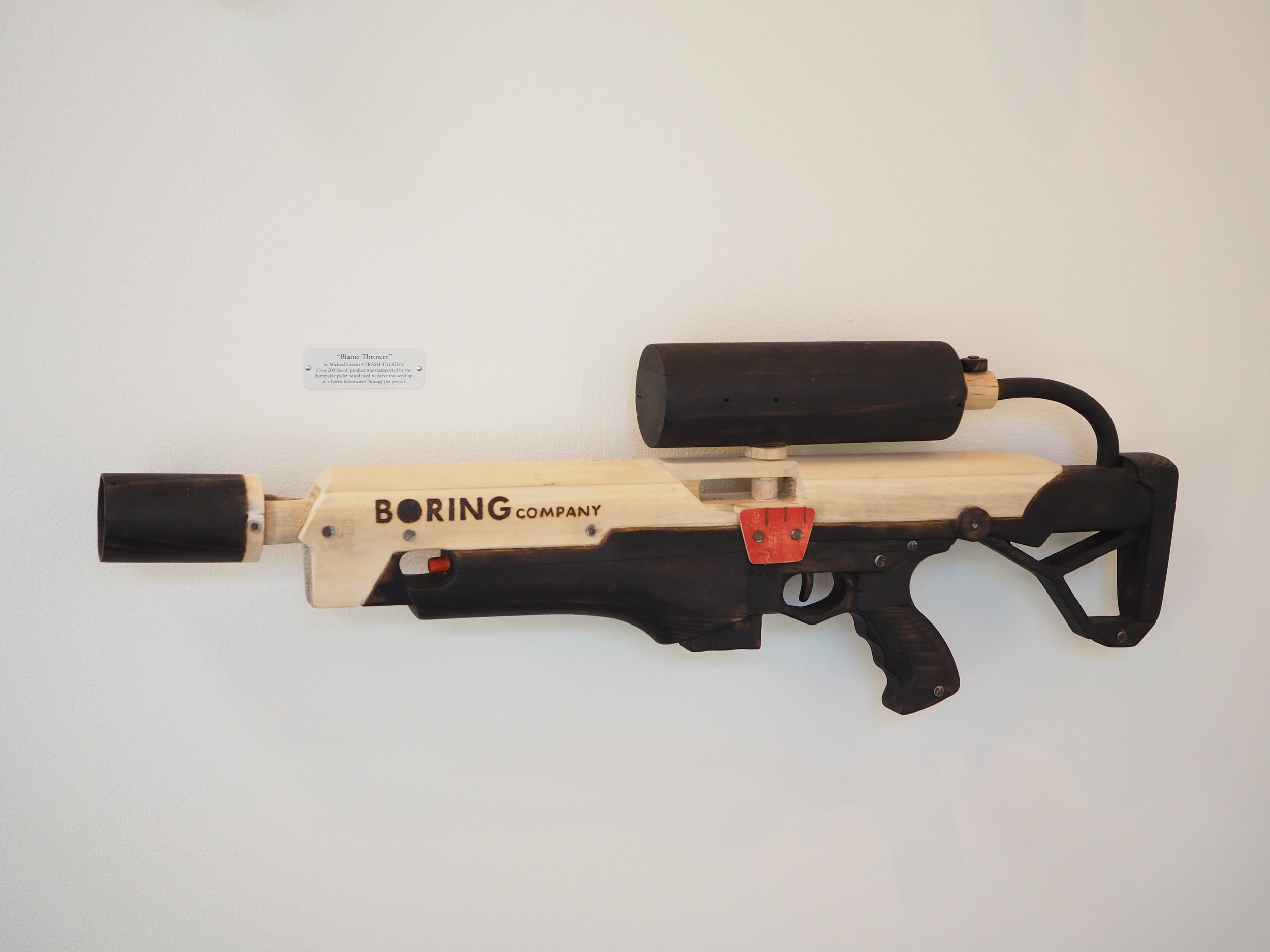 Elon Musk Boring Company flame thrower Twitter X Tesla corporate culture anti-capitalist woodworking wood sculpture recycled reclaimed pallet wood satire celebrity parody art