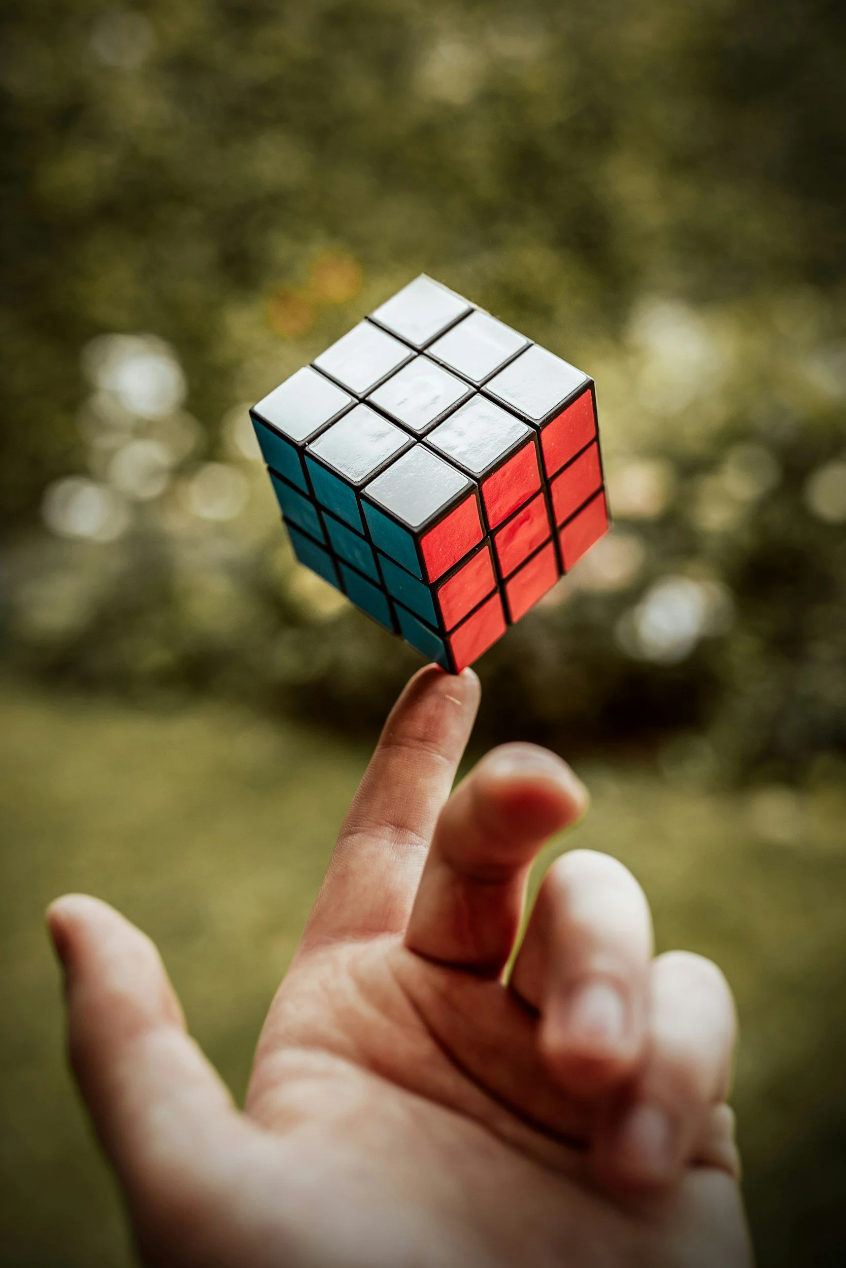 A hand holding a partially solved Rubik's Cube outdoors with a blurred natural background.