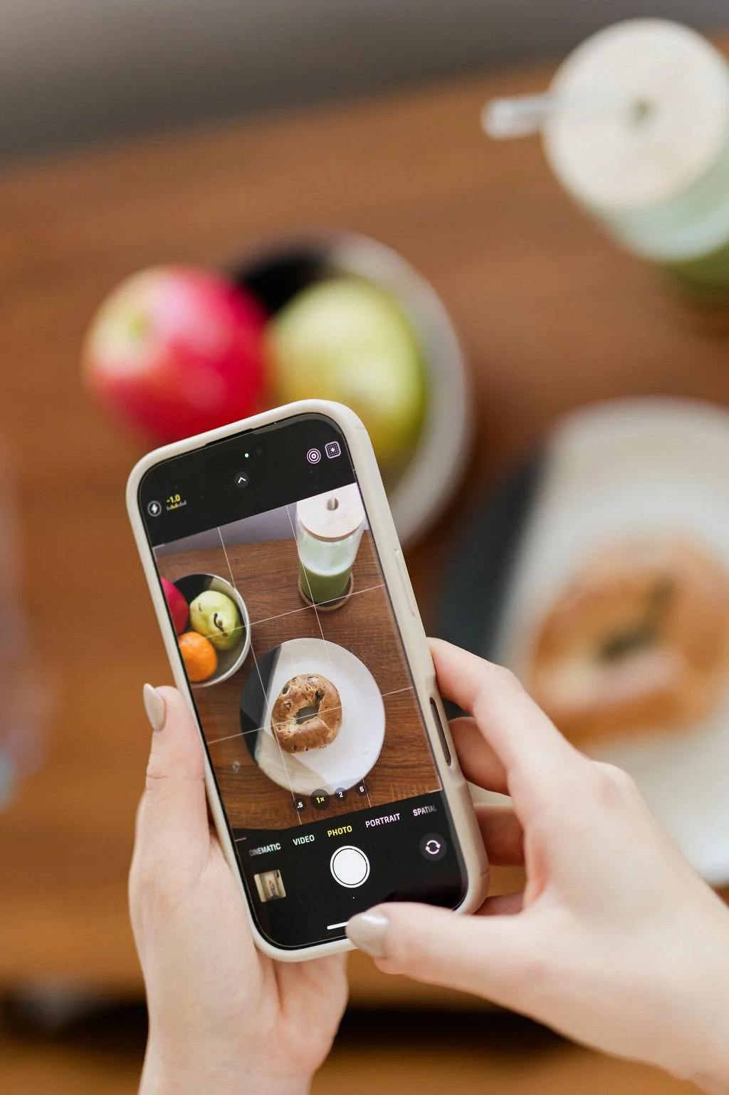 Chloe Cox, host of recovered-ish with chloe cox podcast is taking a picture of a bagel, fruit, and matcha on her phone.