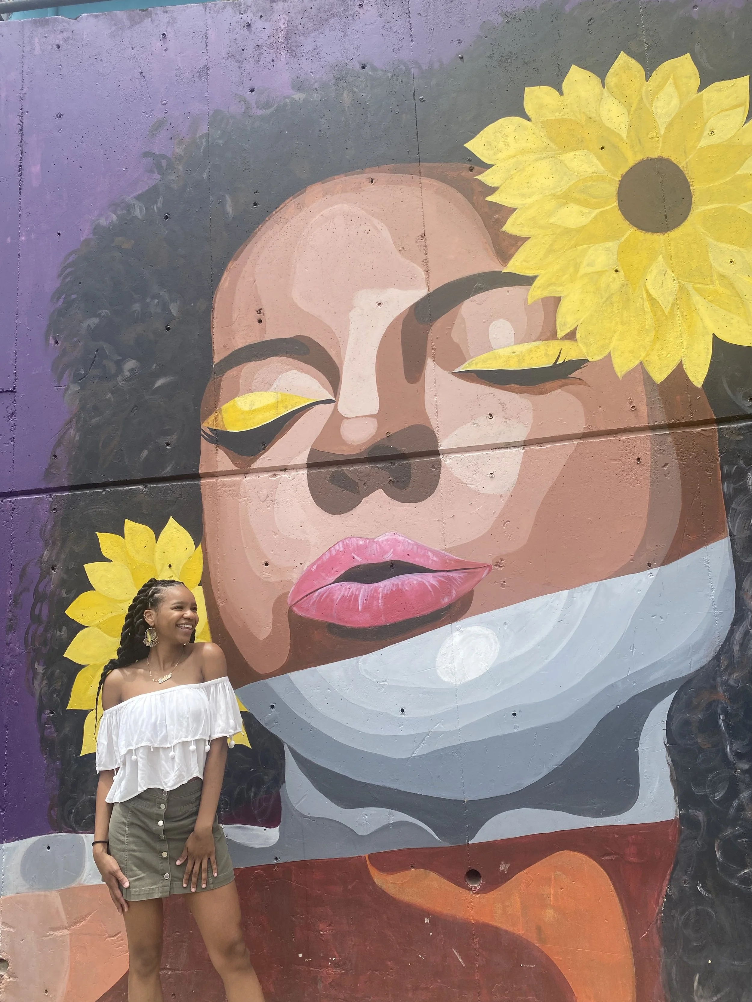 A black girl standing in front of a mural of a black woman