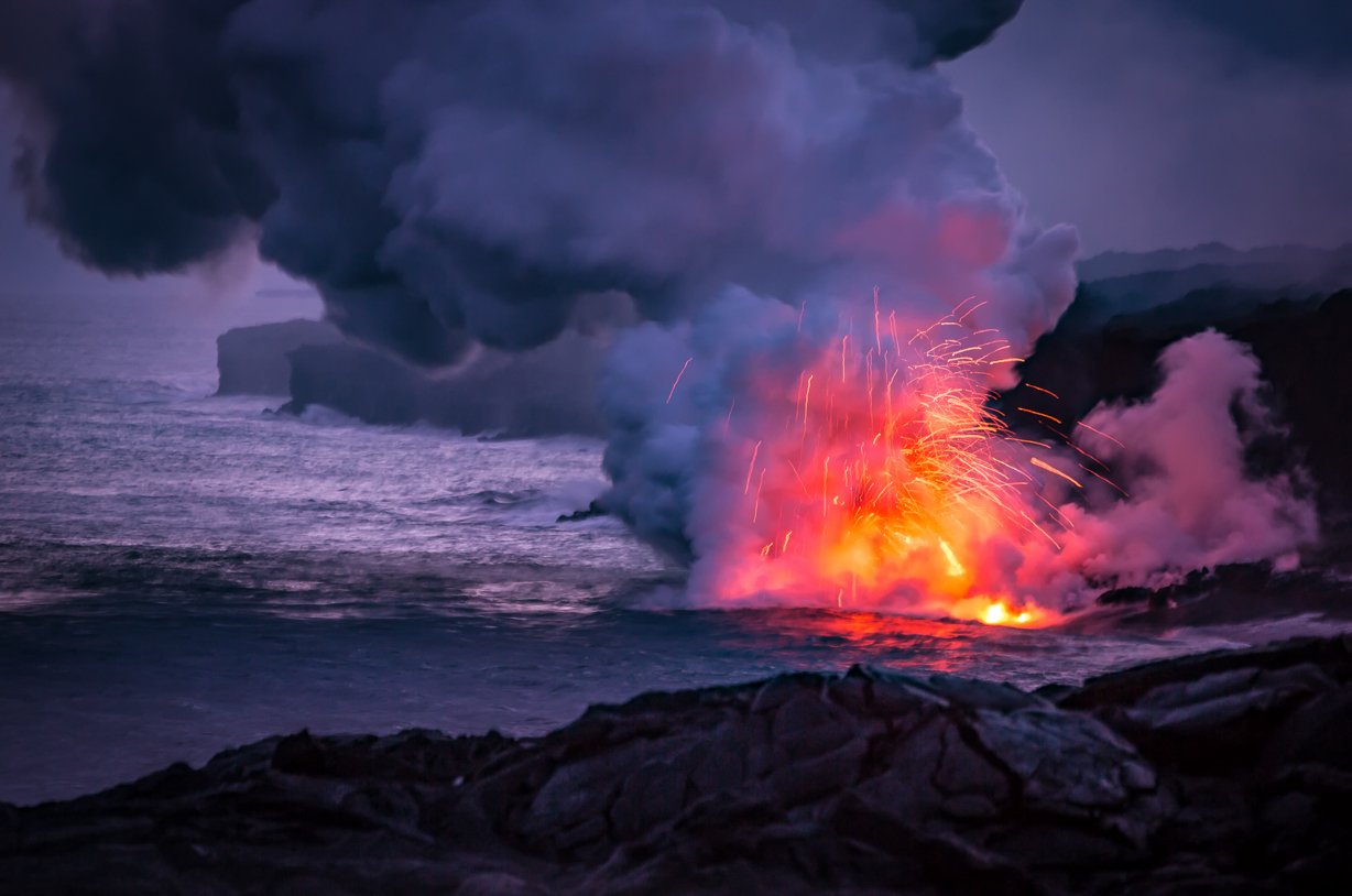 fresh lava spews into the ocean creating a fireworks display as it touches the water