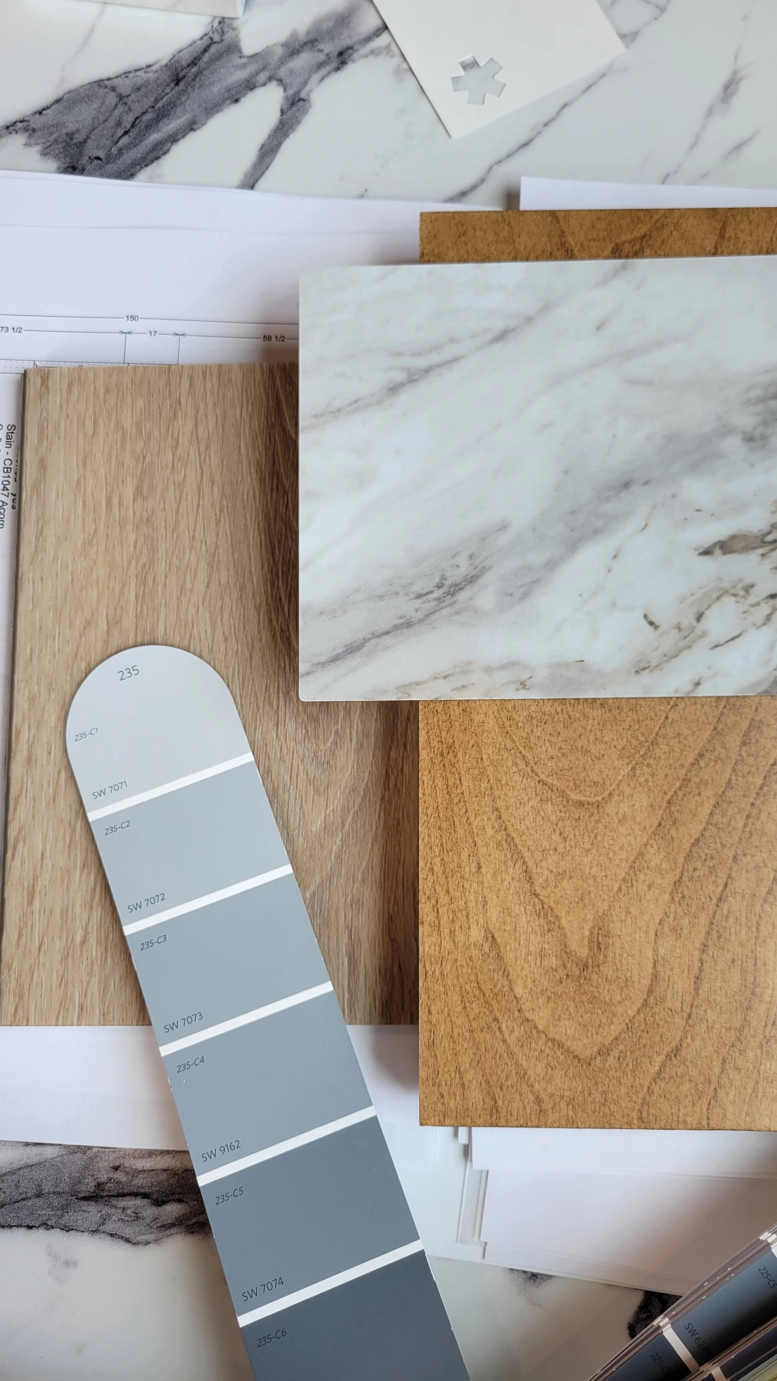 Sample of various interior design materials including marble, wood grains, and paint color swatches arranged on a marble surface.