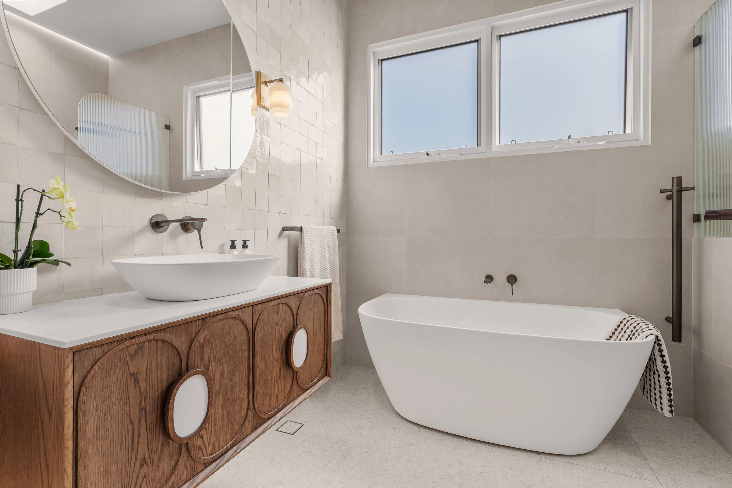 Art Deco-inspired curves and timber joinery bring character into a clean, contemporary bathroom.