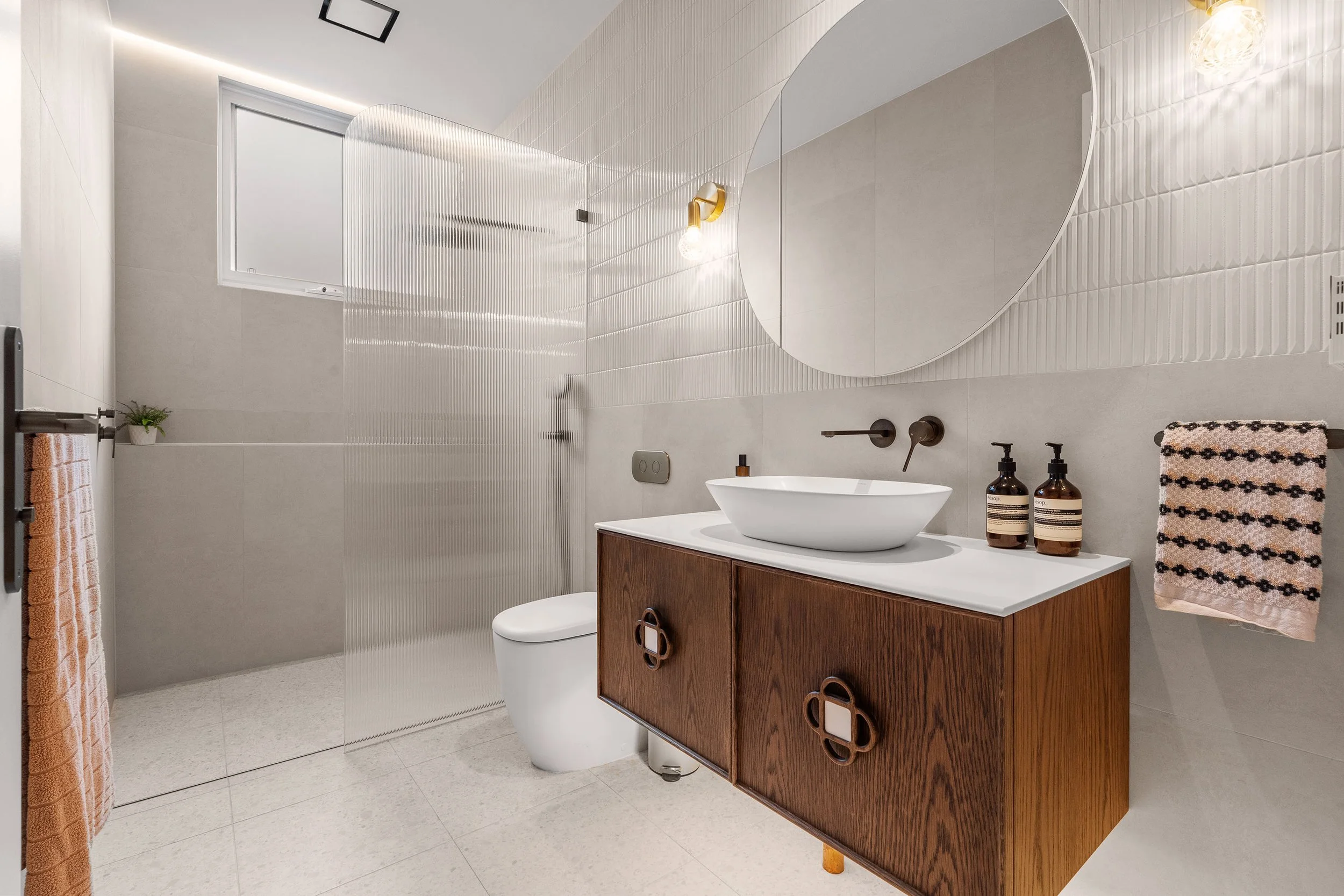 Textured tiles, fluted glass and warm timber bring softness and character to this contemporary bathroom.