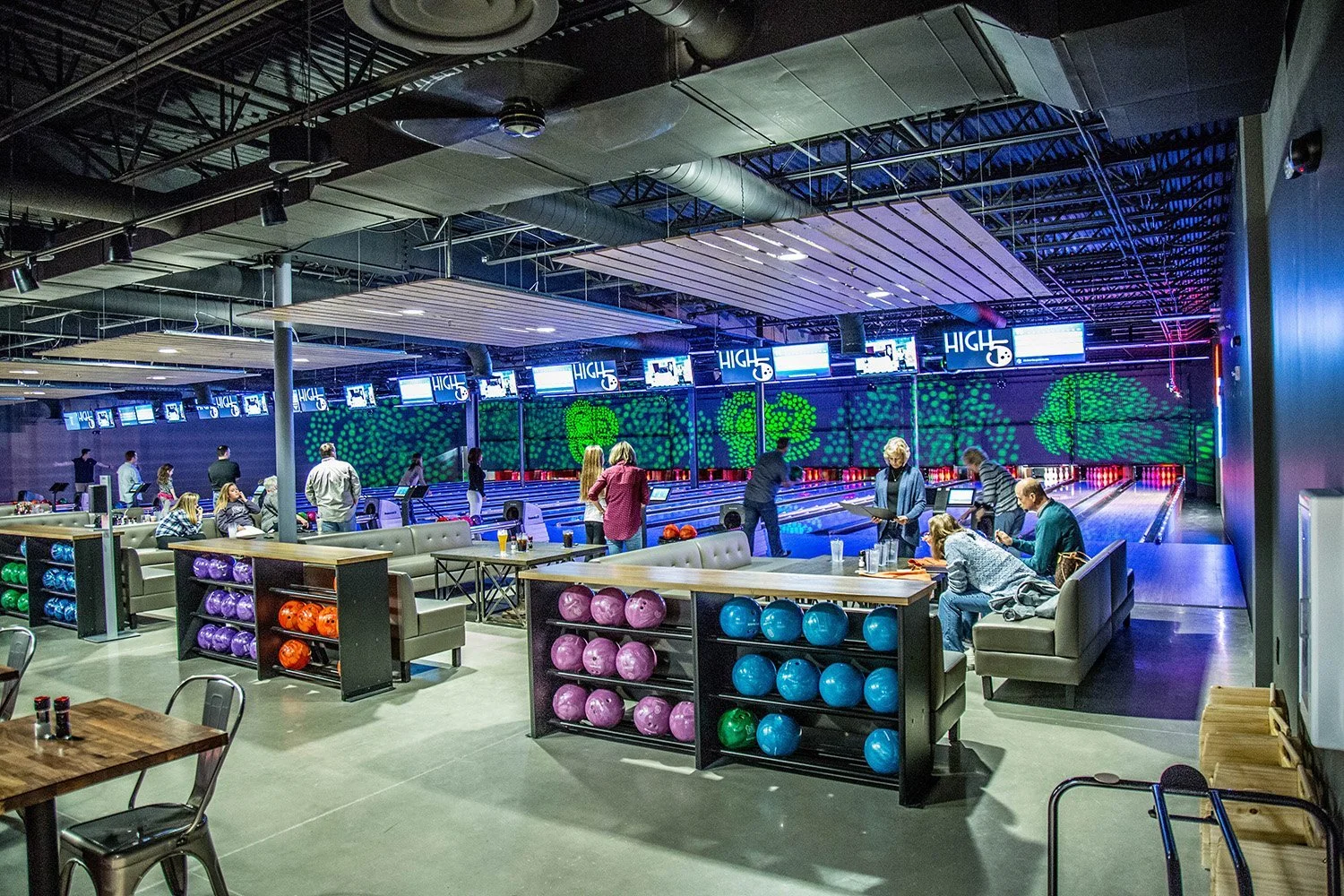 People playing bowling in an indoor alley with colorful bowling balls and digital screens overhead.