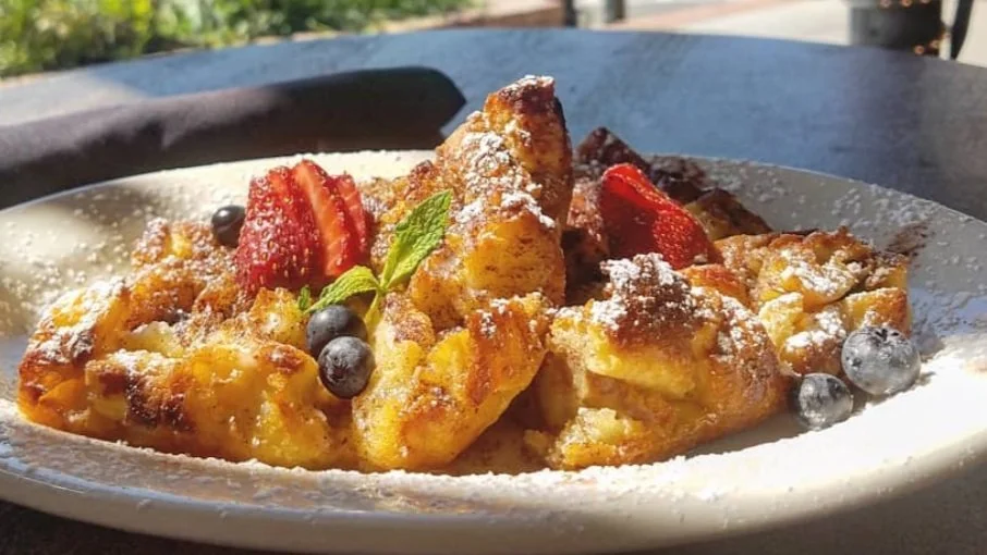 French toast topped with strawberries, blueberries, powdered sugar, and a sprig of mint on a white plate.
