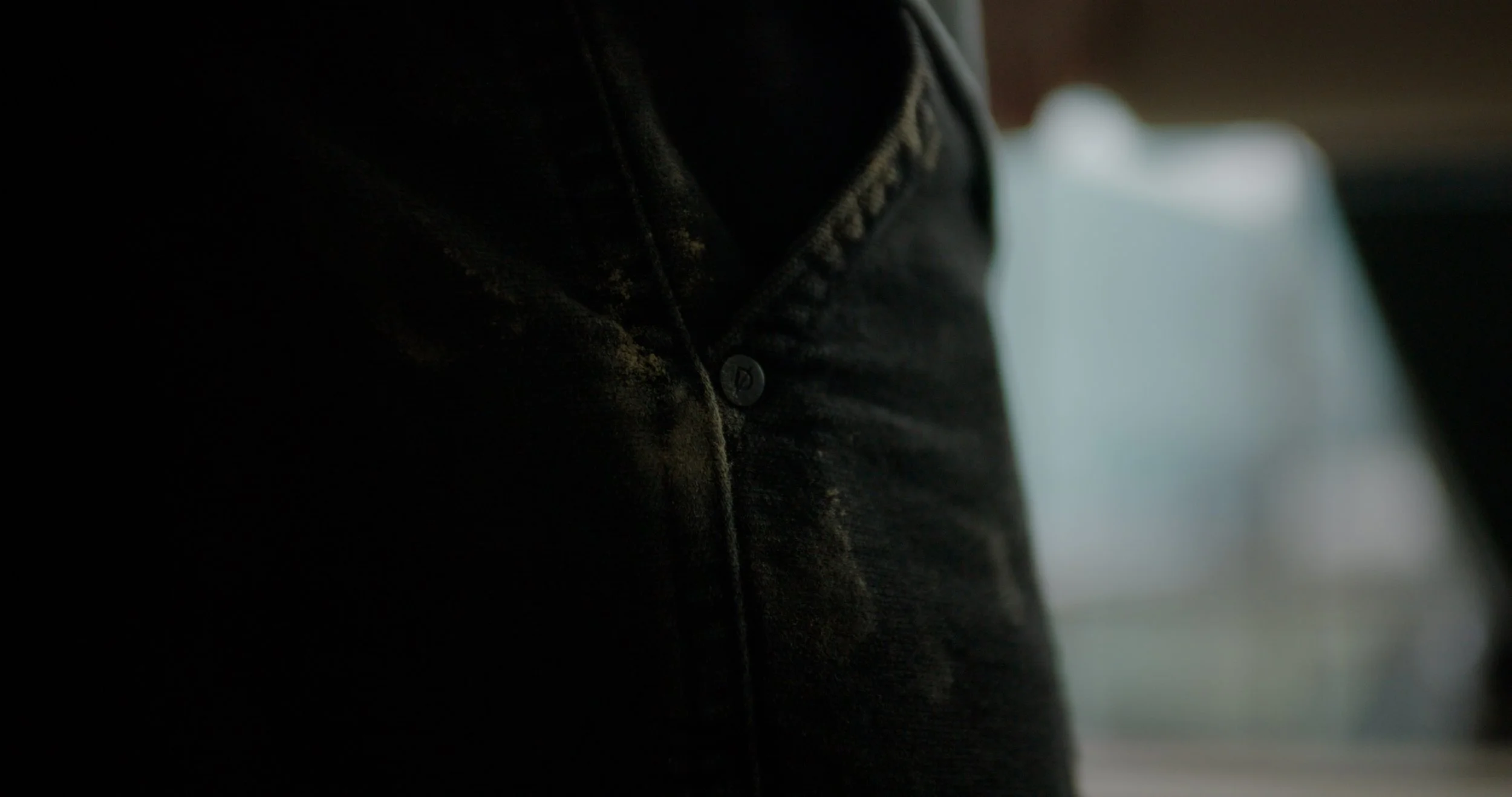 Close-up of a black denim shirt buttoned up, with a blurred background.