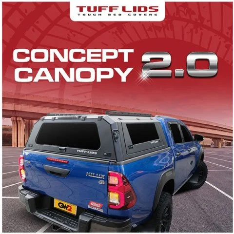 Promotional image for Tuff Lids Concept Canopy 2.0, showing a blue Toyota Hilux pickup truck from a rear three-quarter view, fitted with a black Tuff Lids canopy. The truck is parked in an outdoor lot with an overpass or bridge in the background. Lar