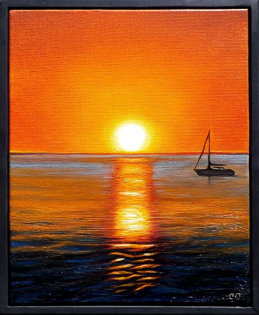 Sunset over the ocean with a sailboat on the right, reflecting orange and yellow hues on the water.