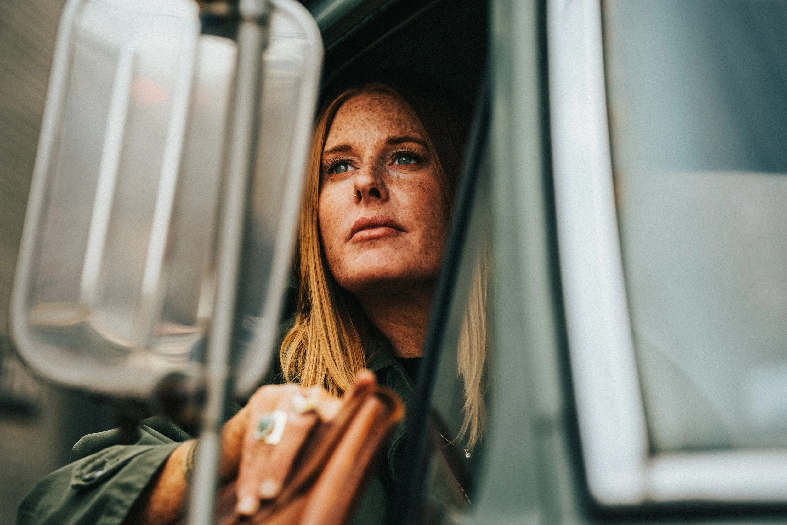 A woman with red hair and freckles looking upward through a vintage truck window.