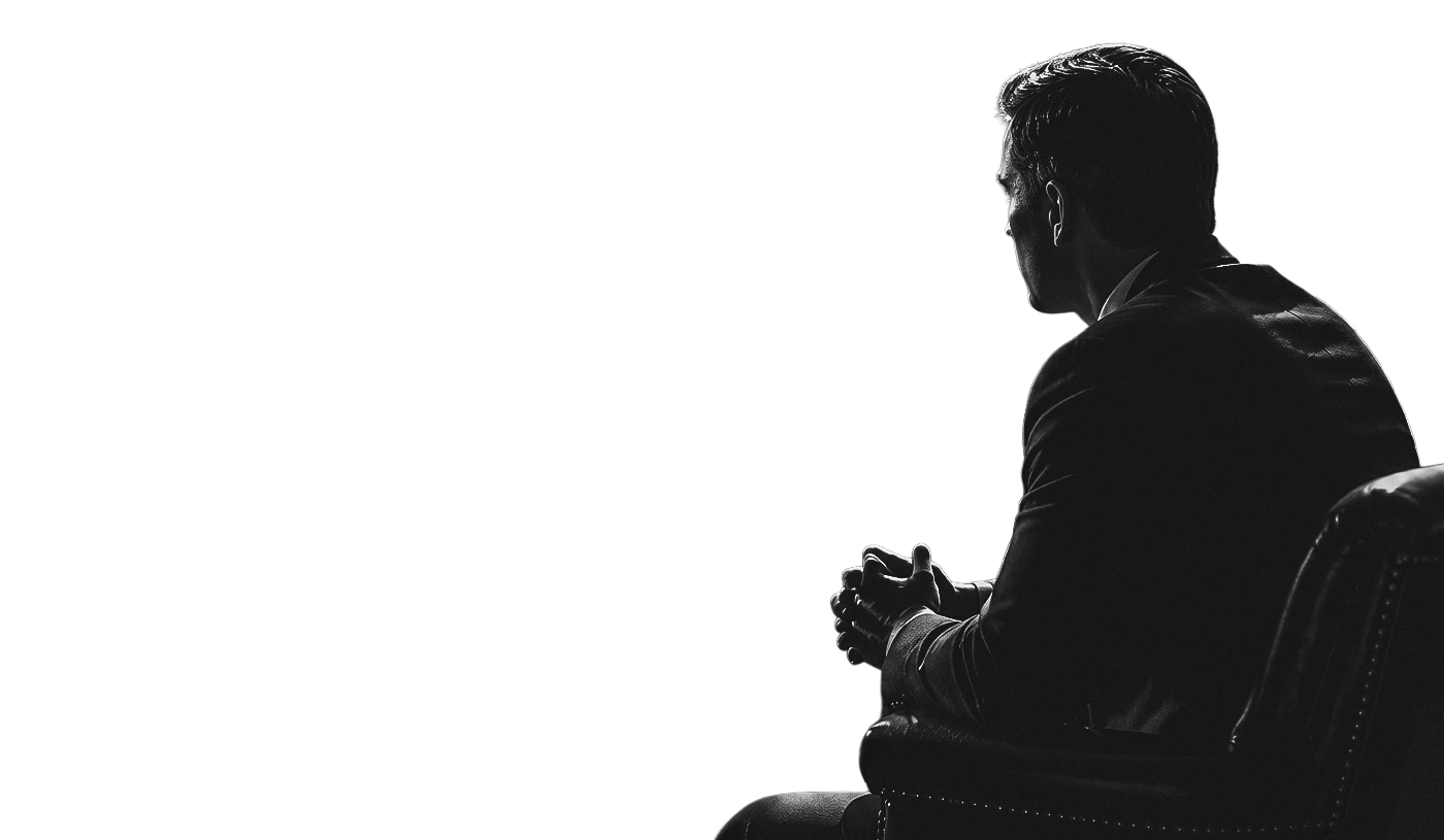 Silhouette of a man sitting with hands clasped, facing sideways, in a dark room.
