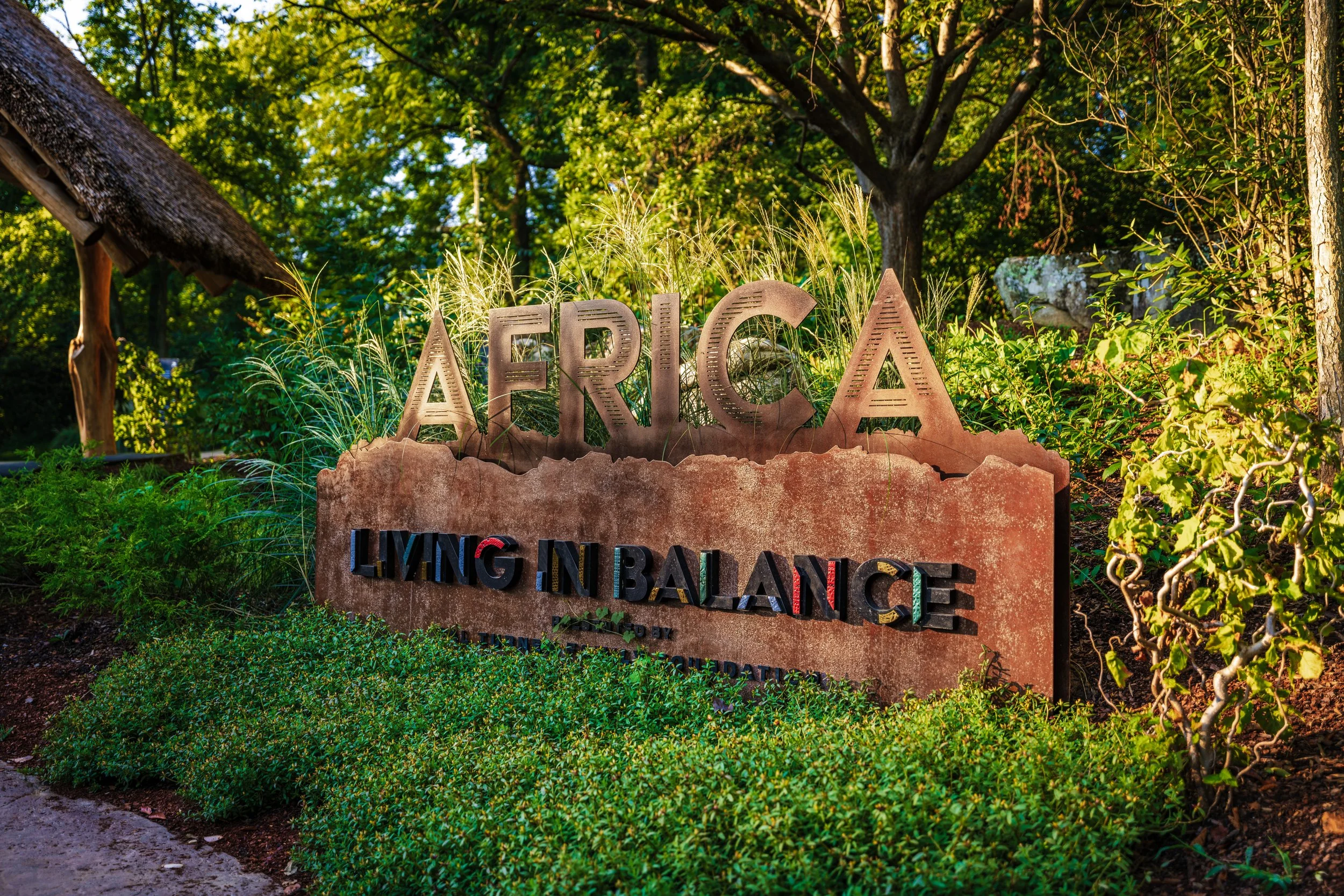 Outdoor sign reading 'AFRICA' and 'LIVING IN BALANCE' set amidst greenery and trees.