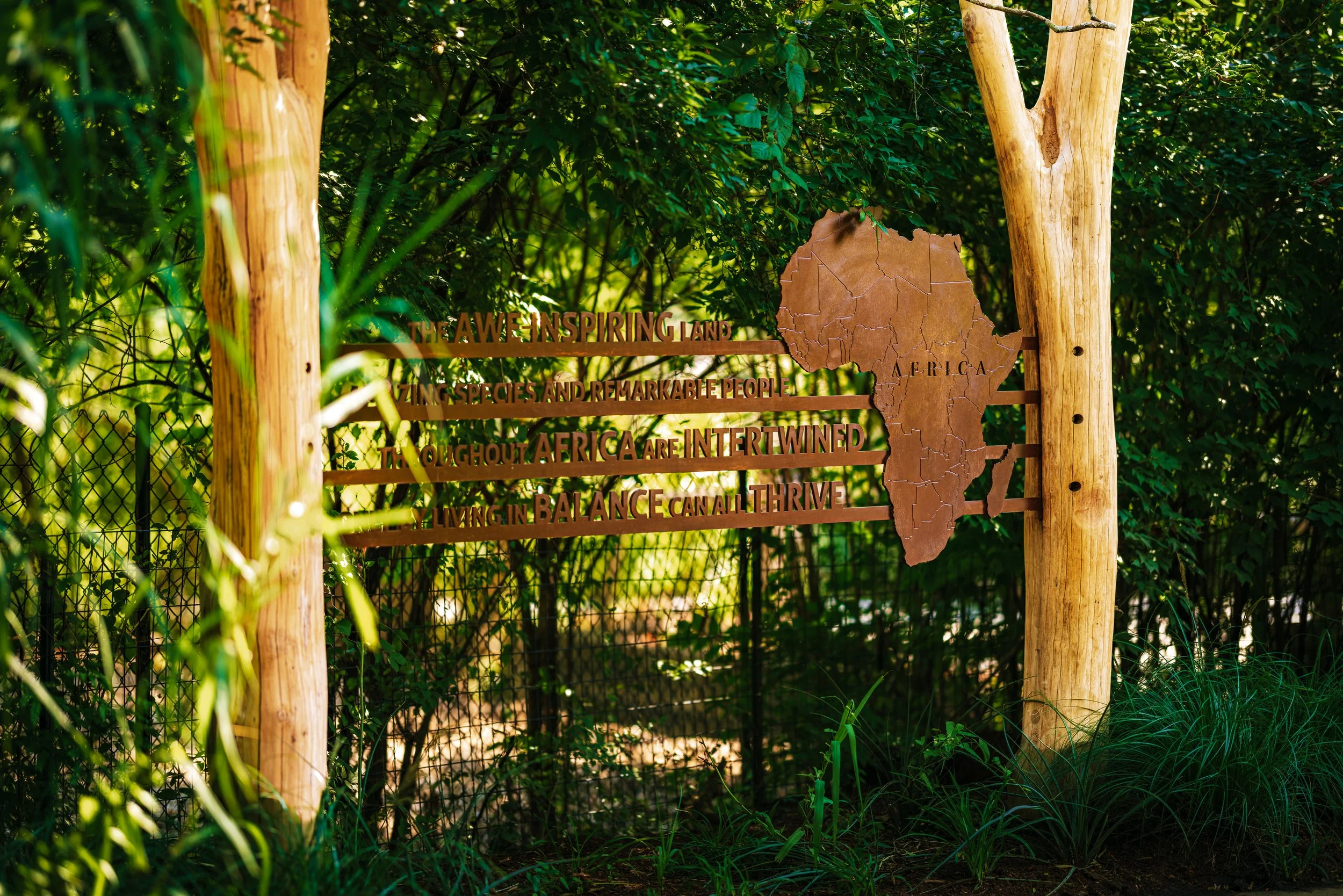 A wooden sign with cutout map of Africa and text about Africa's biodiversity, surrounded by green foliage and trees.