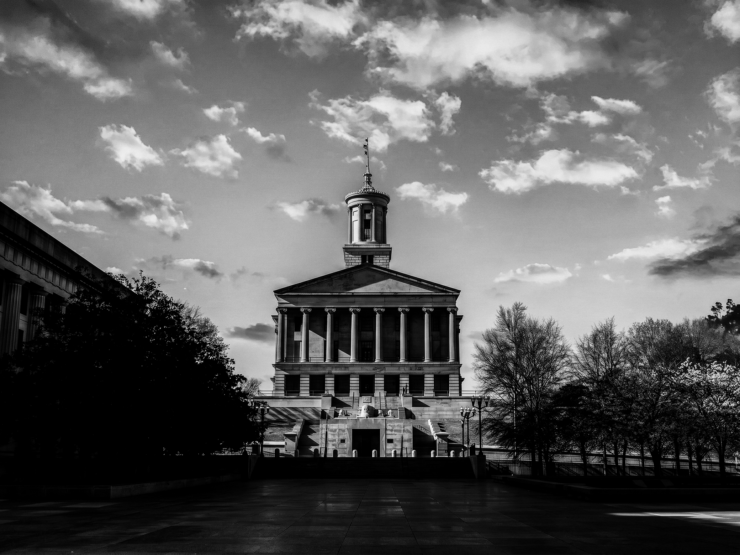 Black and white photo of the Tennessee State Capitol building, trees in the foreground, and a partly cloudy sky.