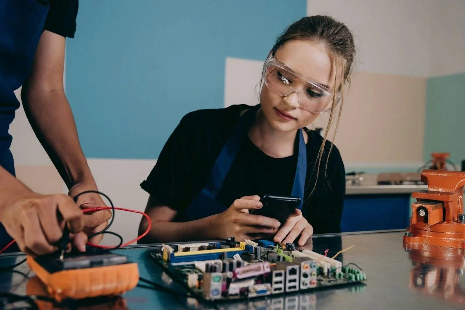 A woman with goggles works with her partner on computer hardware.
