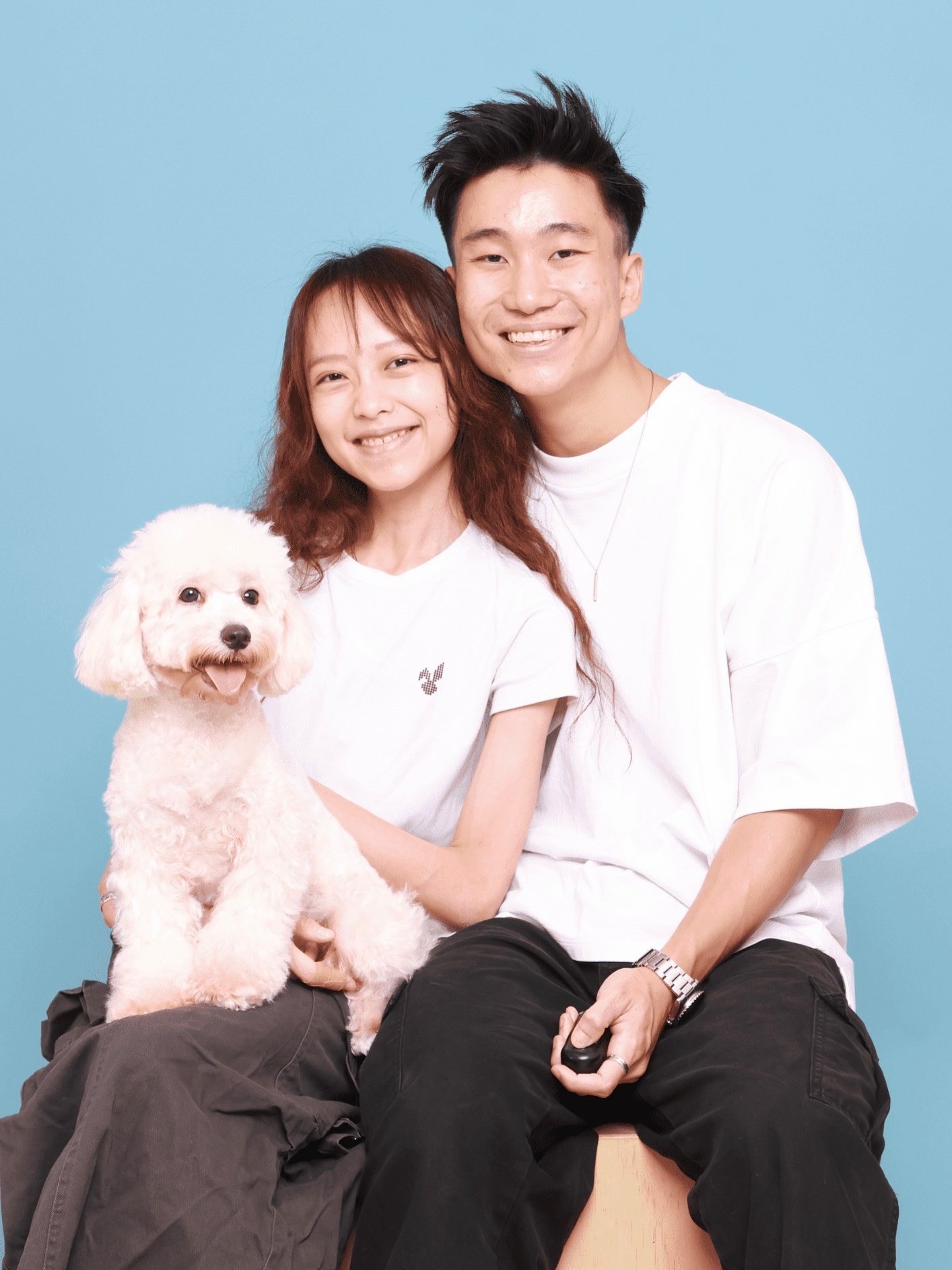 Smiling couple with a small fluffy white dog against a blue background