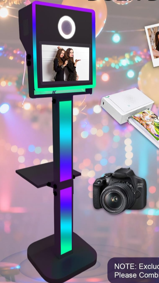 A photo booth stand with a screen showing two women taking a selfie, and a camera, printer, and photo prints nearby, with a blurred background of colorful lights.