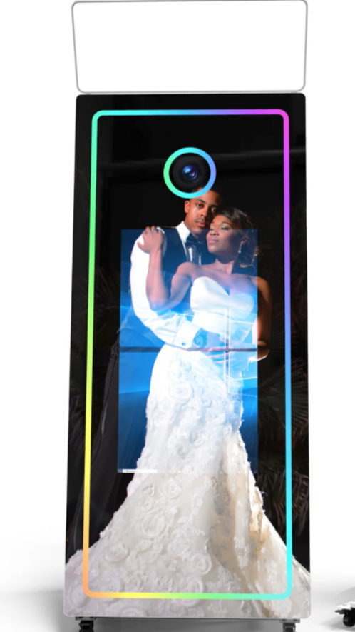 A couple dressed in wedding attire taking a selfie with a holographic mirror image display on a mobile photo booth.