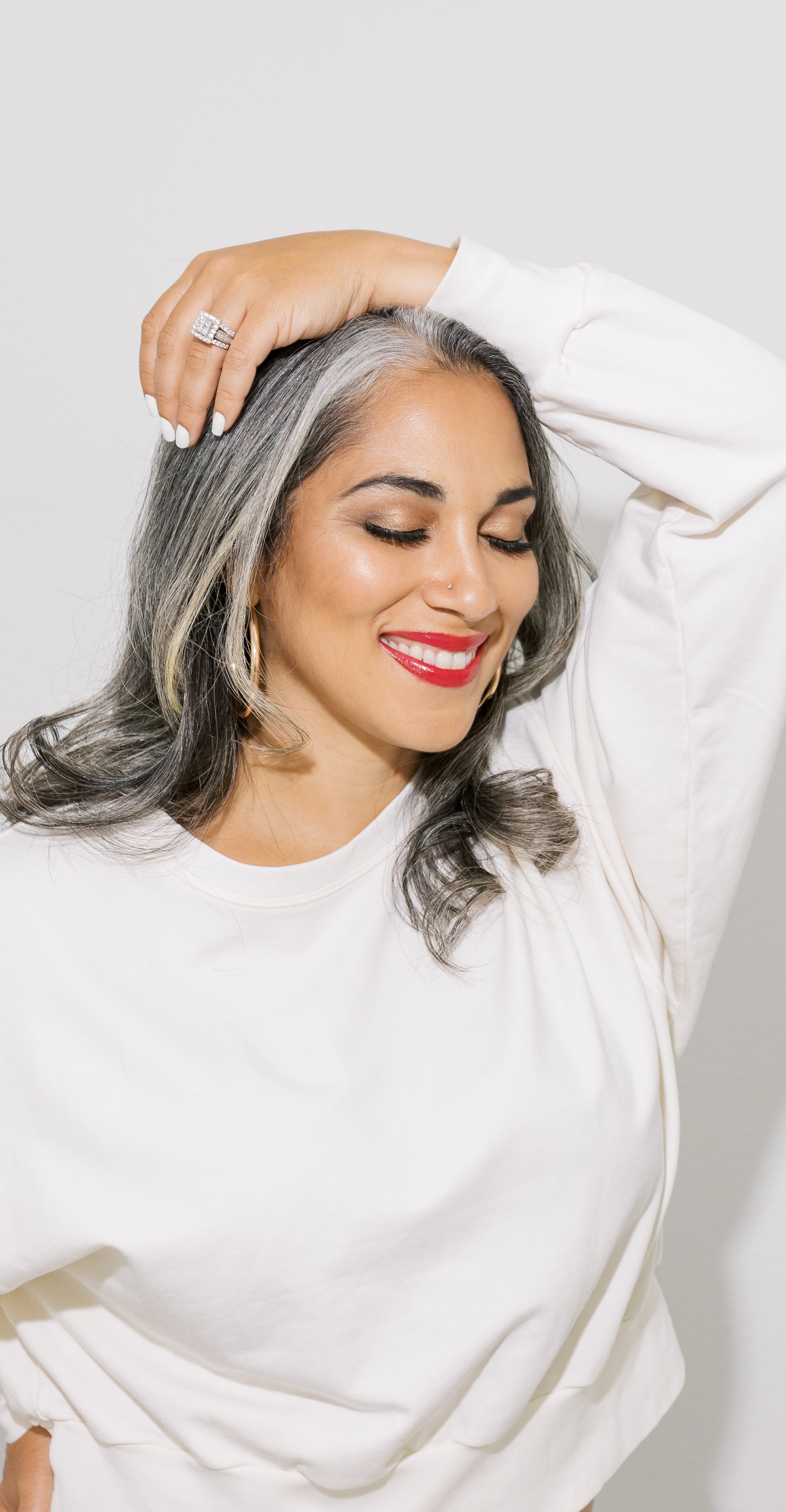 woman smiling posing with hands on top of head in a white sweater