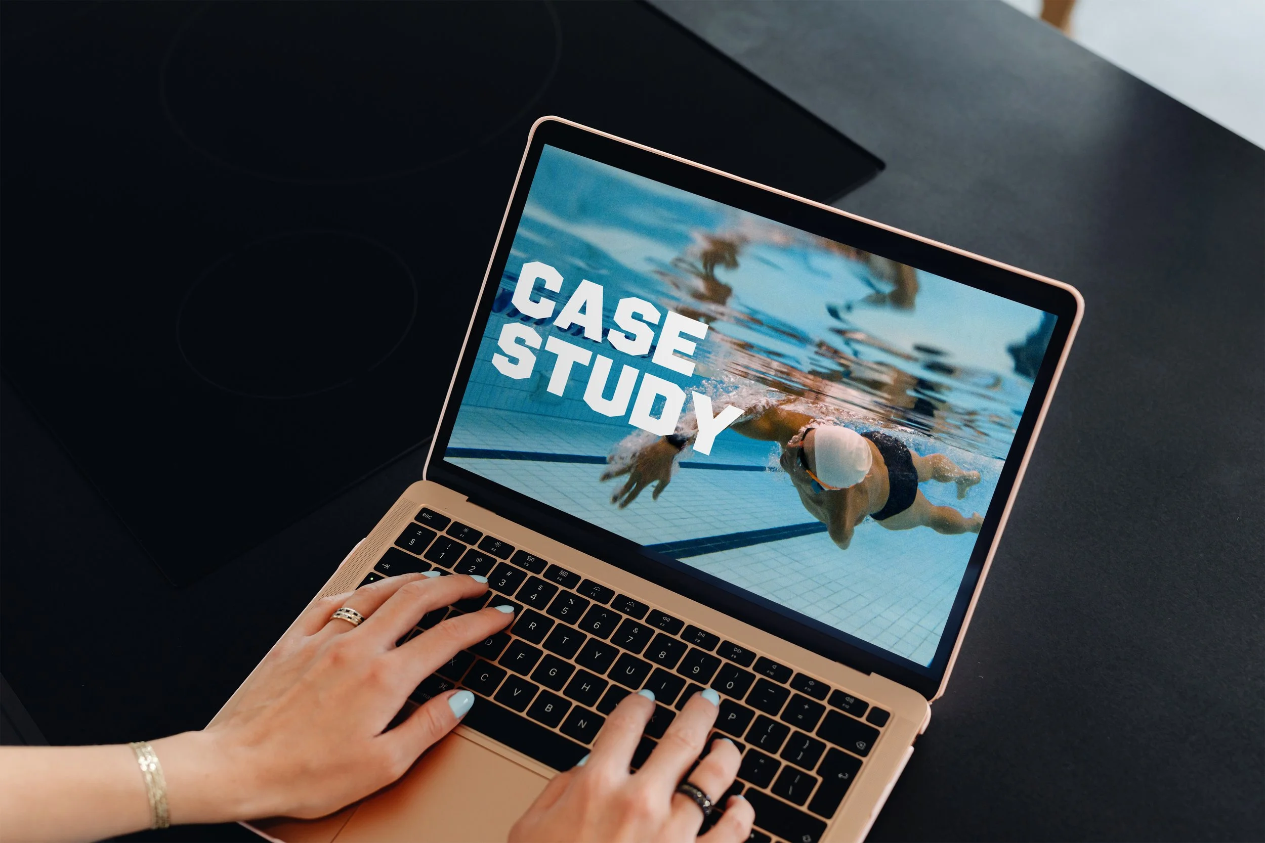 A person with a ring on their finger is typing on a laptop with a screen that displays an image of a swimmer underwater and the words 'CASE STUDY' in bold white letters.