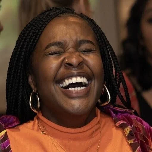 Woman laughing with eyes closed, wearing gold hoop earrings and an orange top.
