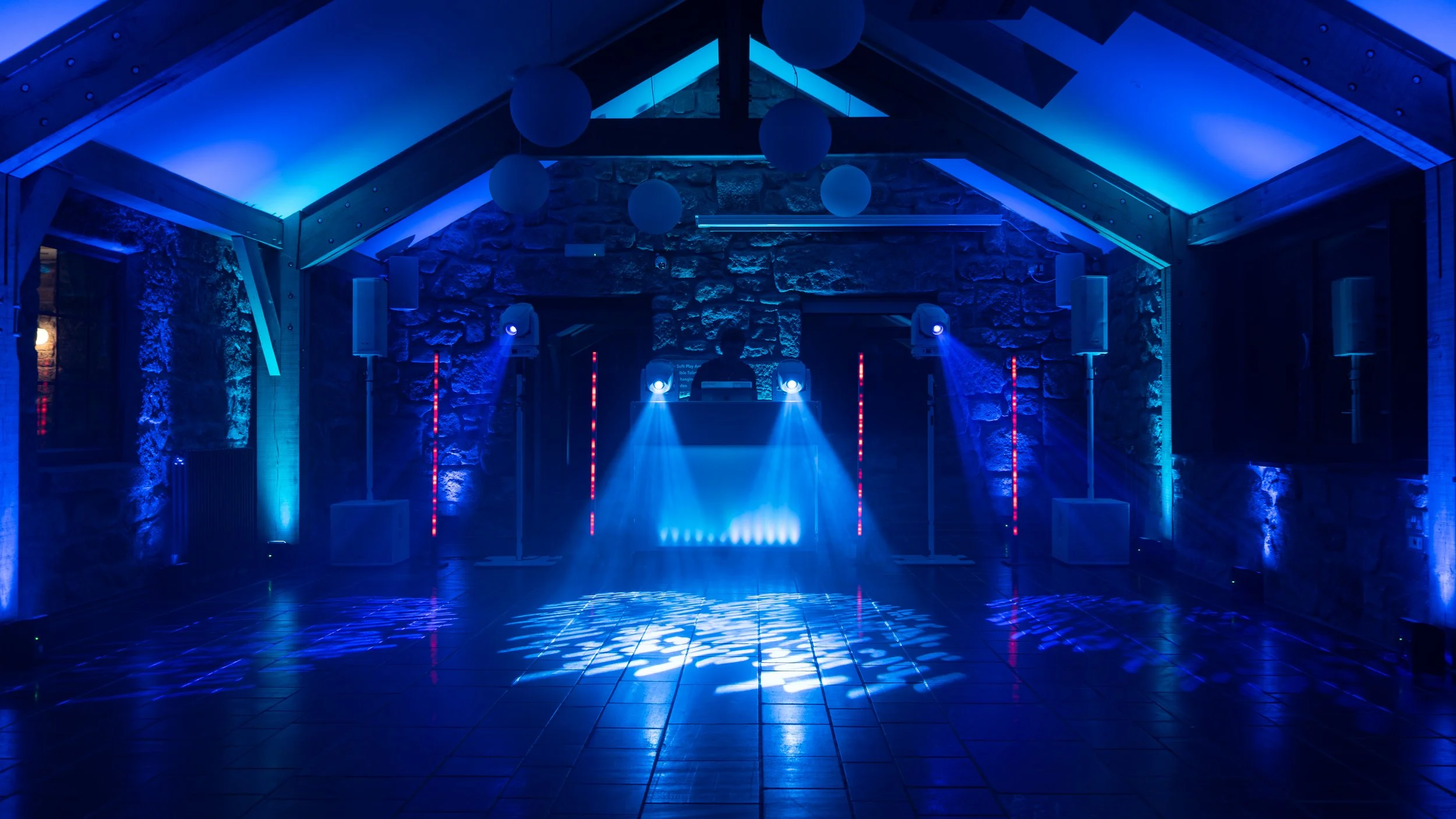 Group of people dancing at a nighttime outdoor event with DJ and colorful lighting.