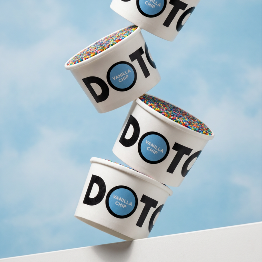 Four cups of vanilla chip ice cream with colorful sprinkles, stacked in a tilted fashion against a blue sky background.