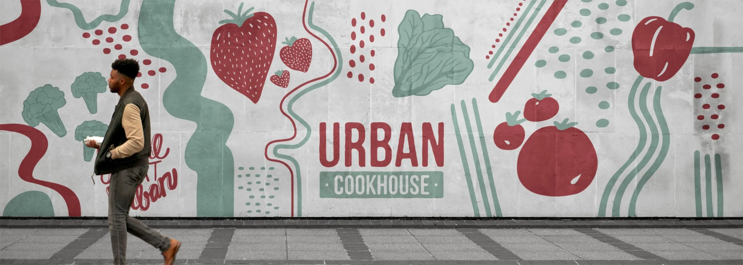 A man walking past a colorful mural with the words "Urban Cookhouse" surrounded by illustrations of vegetables and berries, on a city sidewalk.