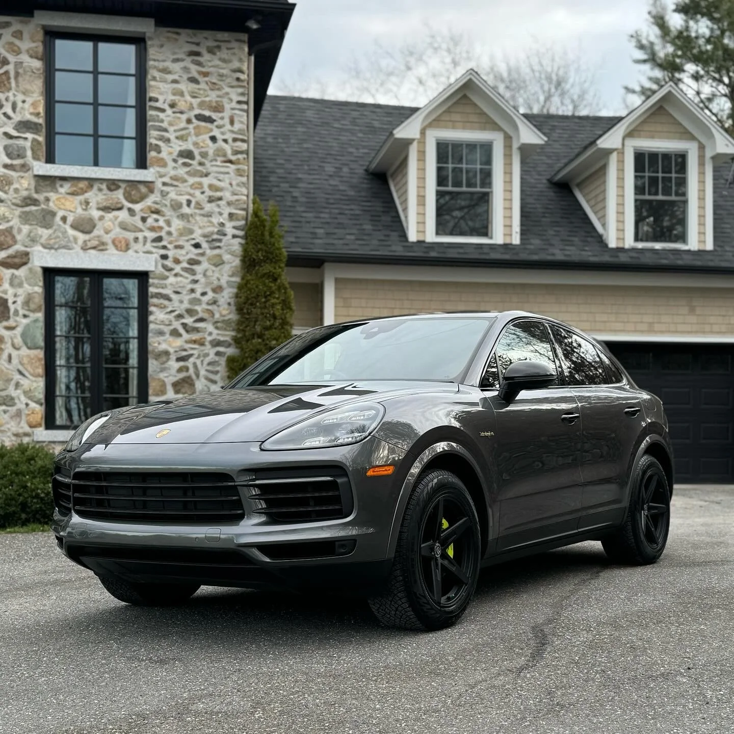 Voiture de sport noire garée devant une maison avec façade en pierre et une maison avec un toit en pente et des fenêtres à dormer.