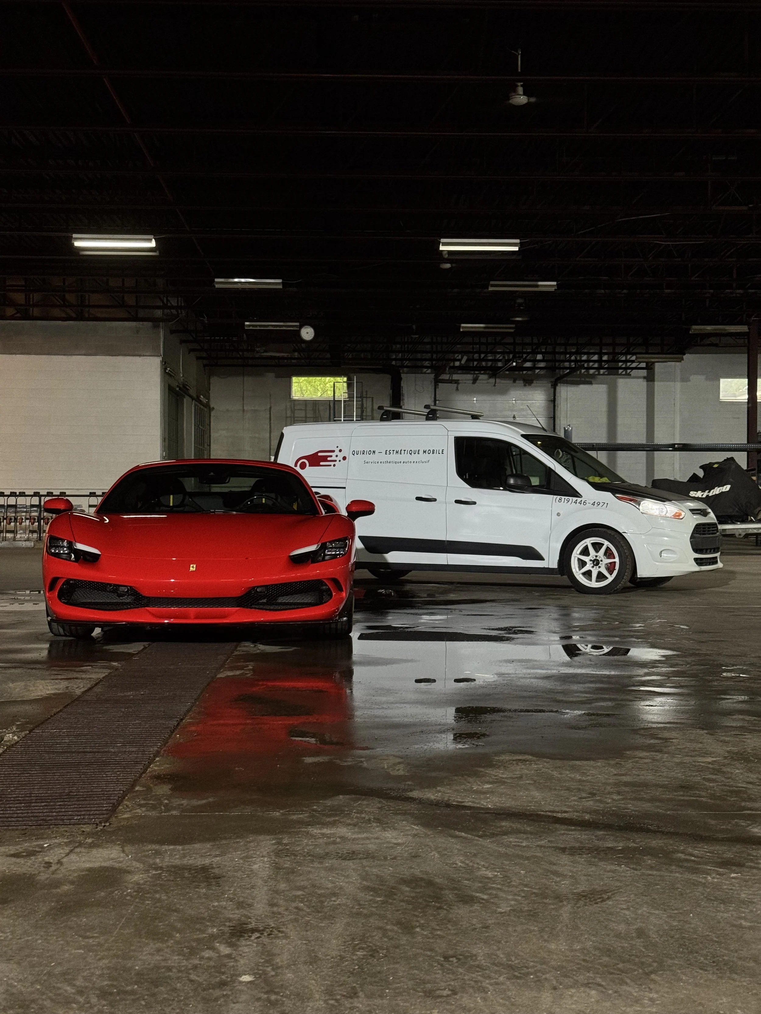 Une voiture Ferrari rouge devant un véhicule utilitaire blanc dans un parking couvert.