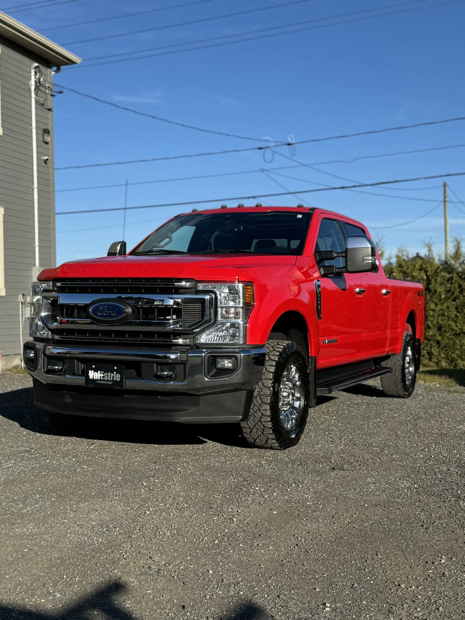Camion rouge Ford F-150 garé sur une surface asphaltée, avec un ciel bleu en arrière-plan.