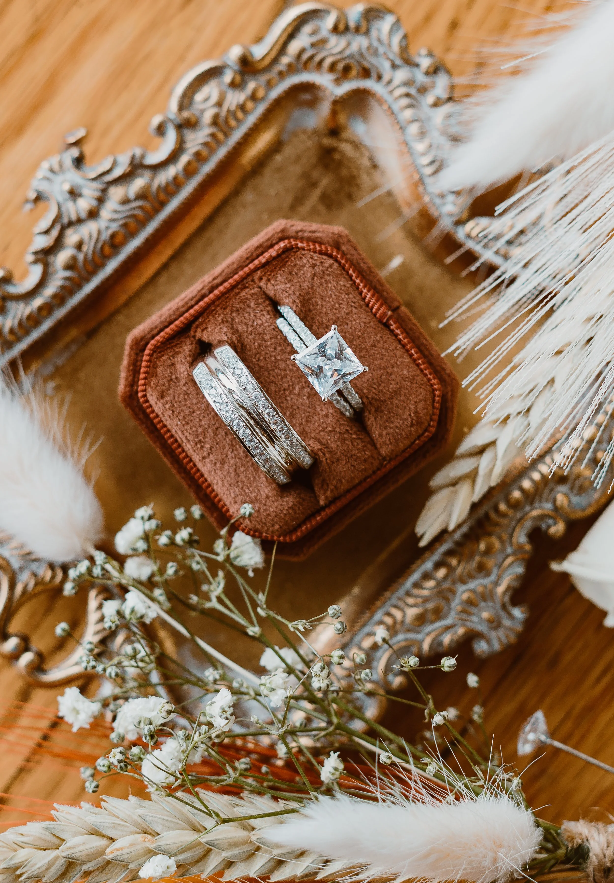 Two rings set in a velvet box on a decorative tray with dried flowers.