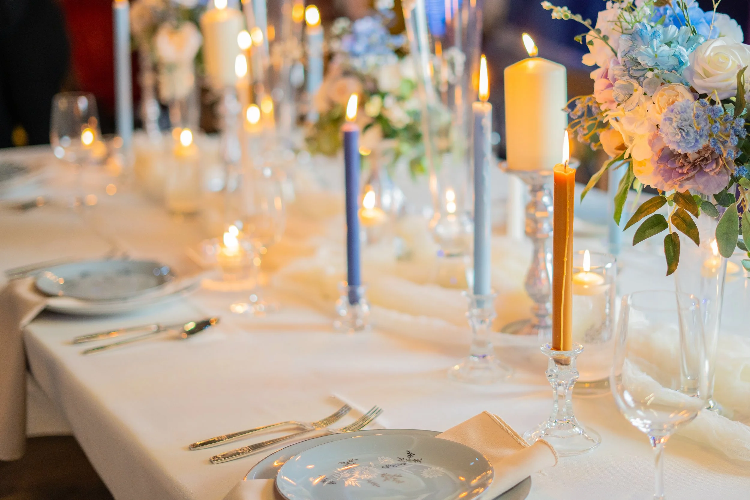 Elegant table setting with lit candles and floral centerpieces on a white tablecloth.