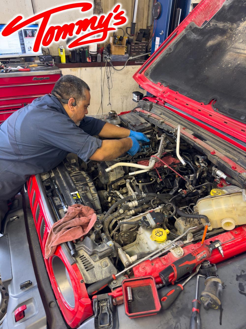 A mechanic working on a car engine in a workshop with tools and equipment around.
