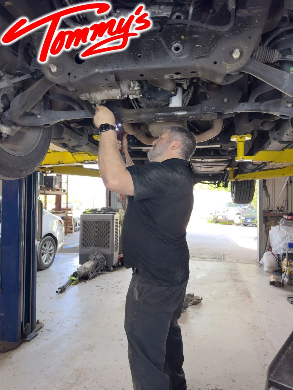 A mechanic working under a lifted car in an auto repair shop.