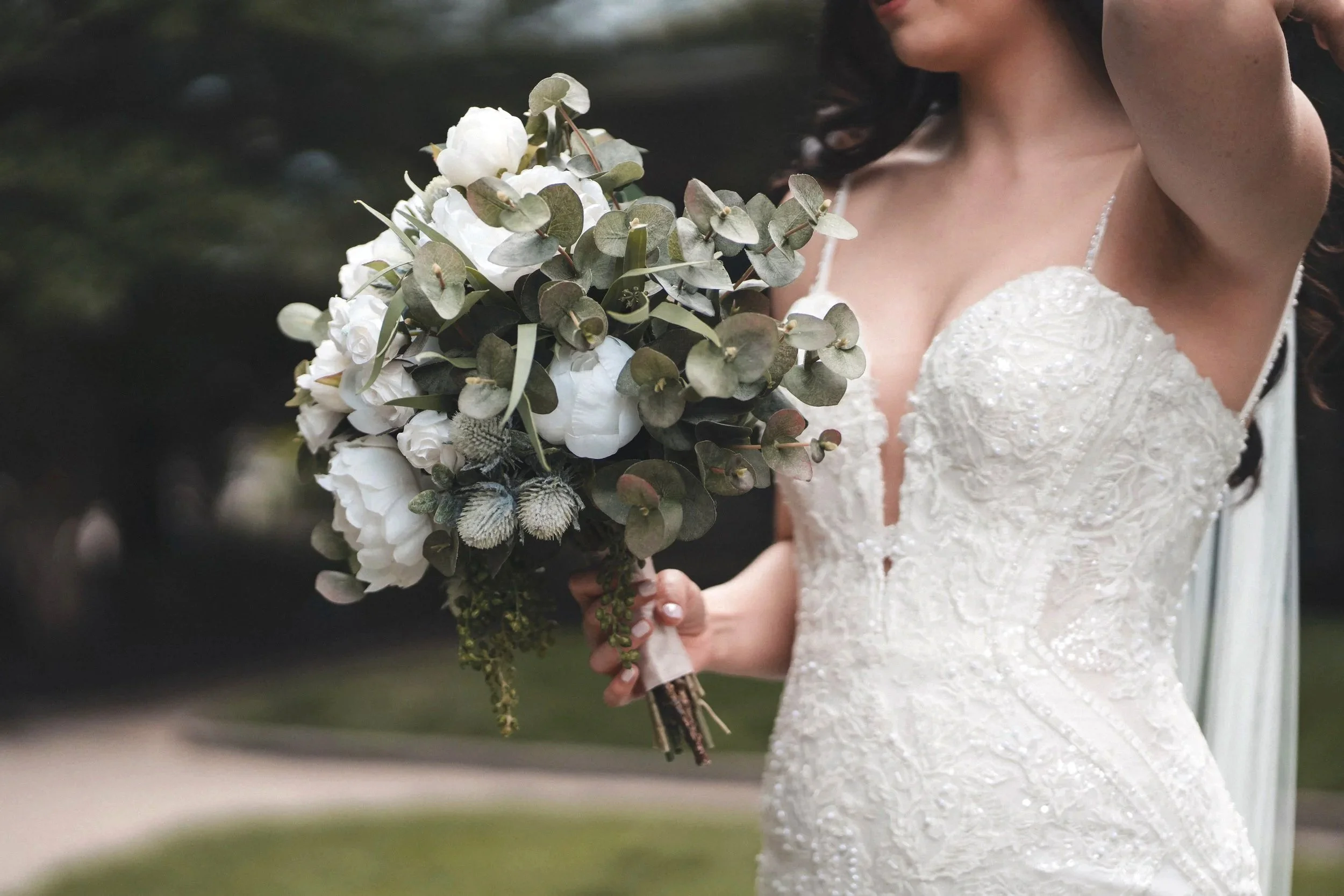 A close-cropped photo of a bride holding a bouquet of peonies and eucalyptus leaves. Her face is out of frame, only her torso is visible, holding the bouquet in her right hand. Taken at the Seaport Hotel in Boston, MA