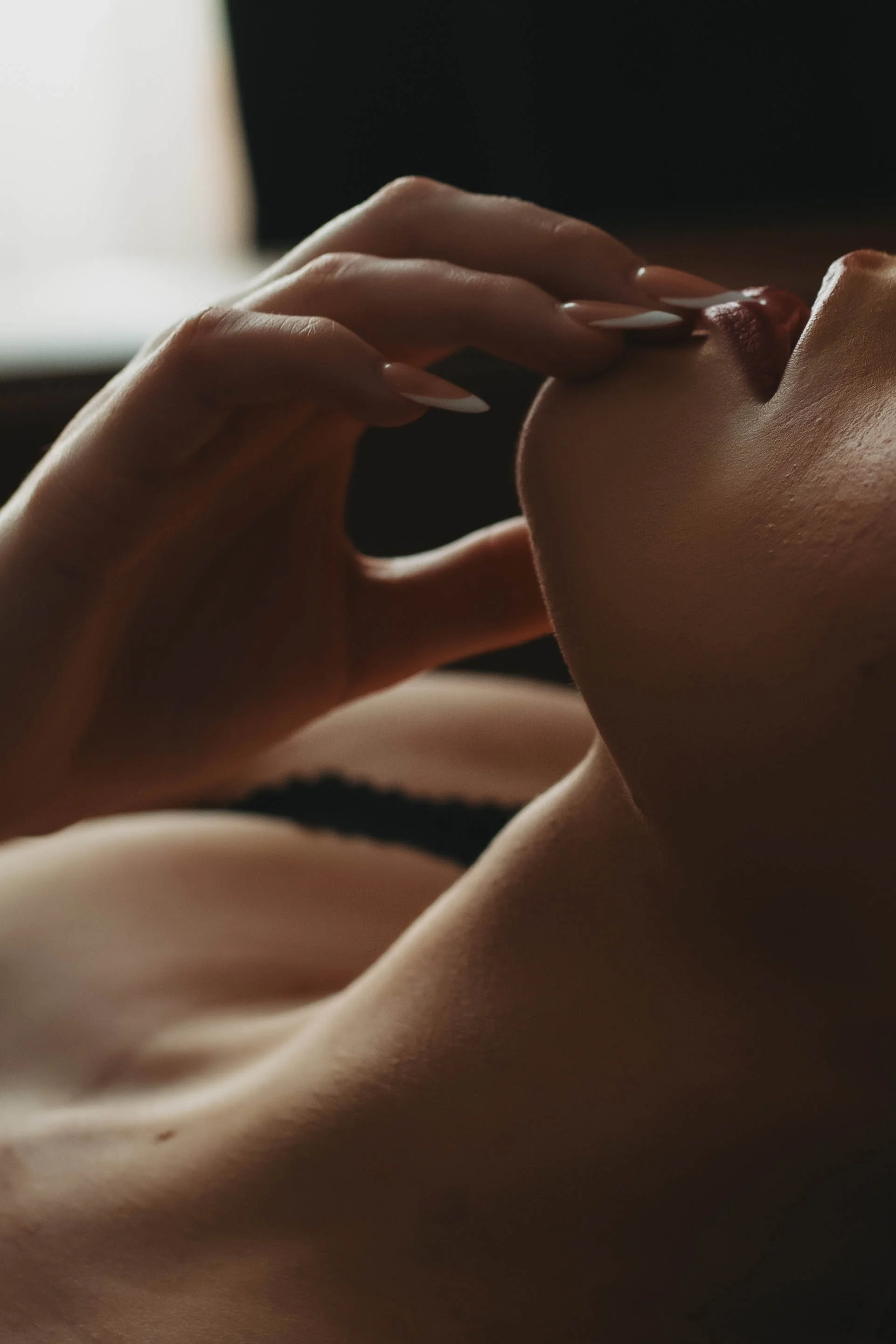 Close-up of a woman touching her lips with her fingers, with soft lighting highlighting her skin and face.