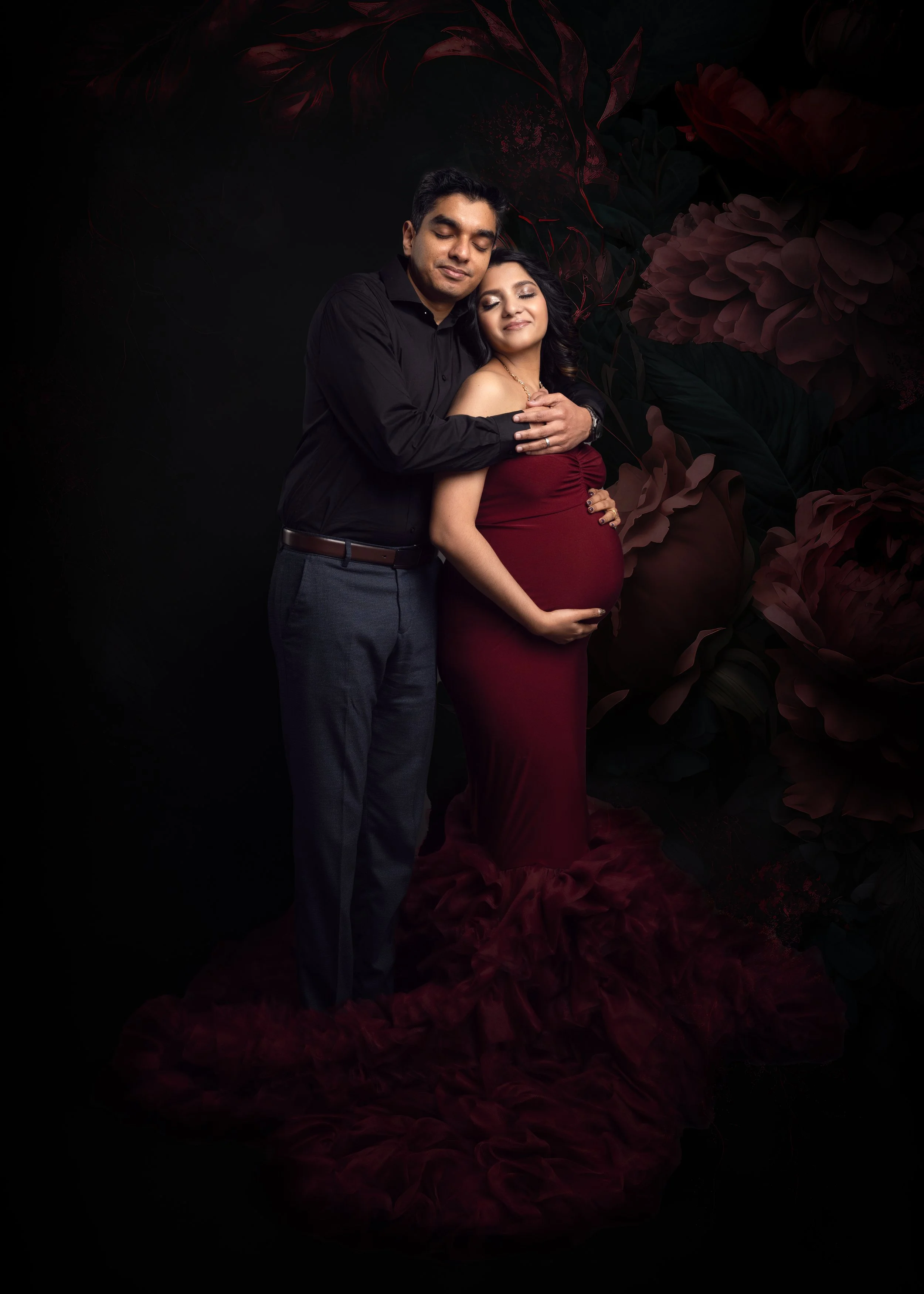 A pregnant woman in red dress posing with her husband for maternity photography