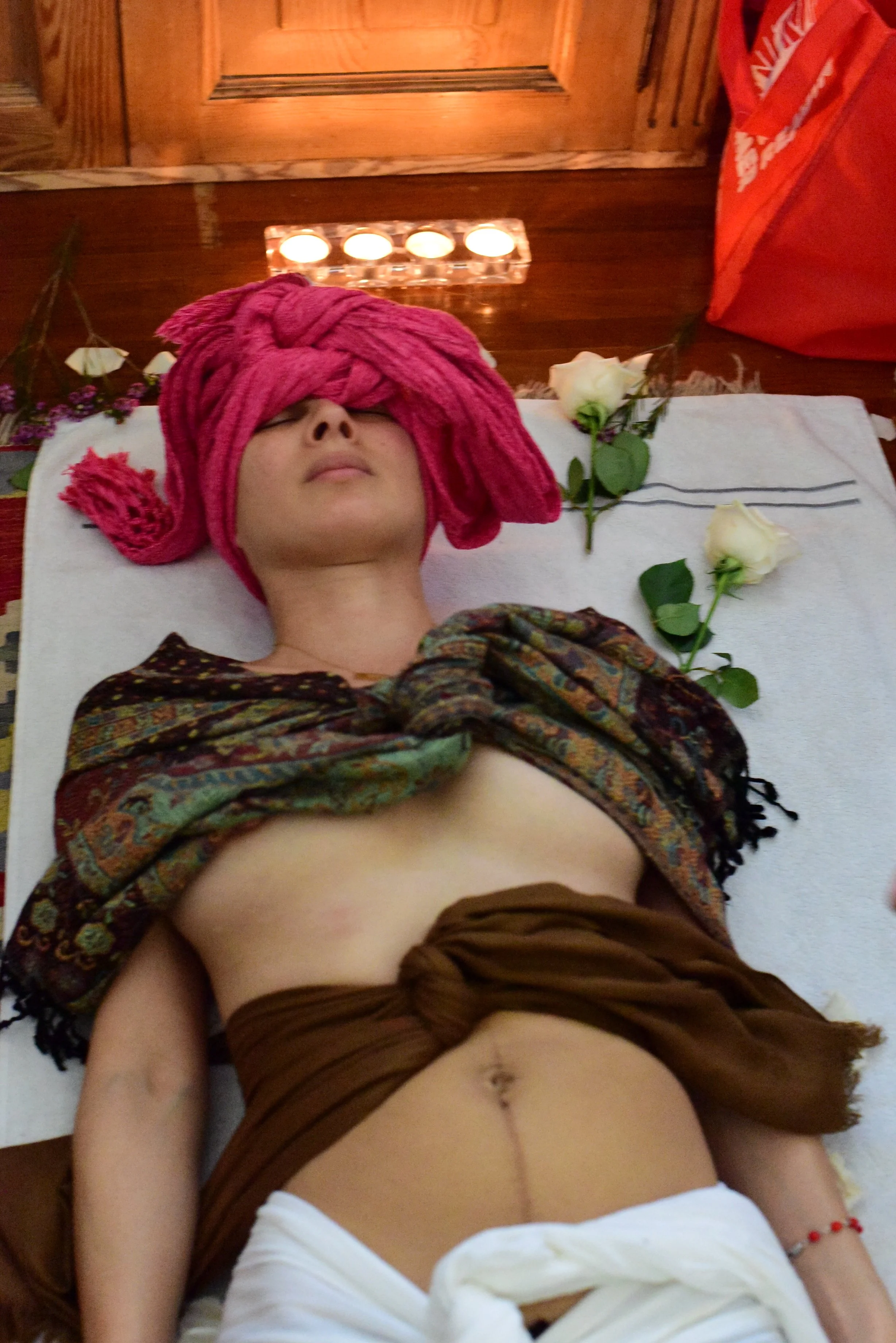 woman laying on a white sheet wrapped in scarfs