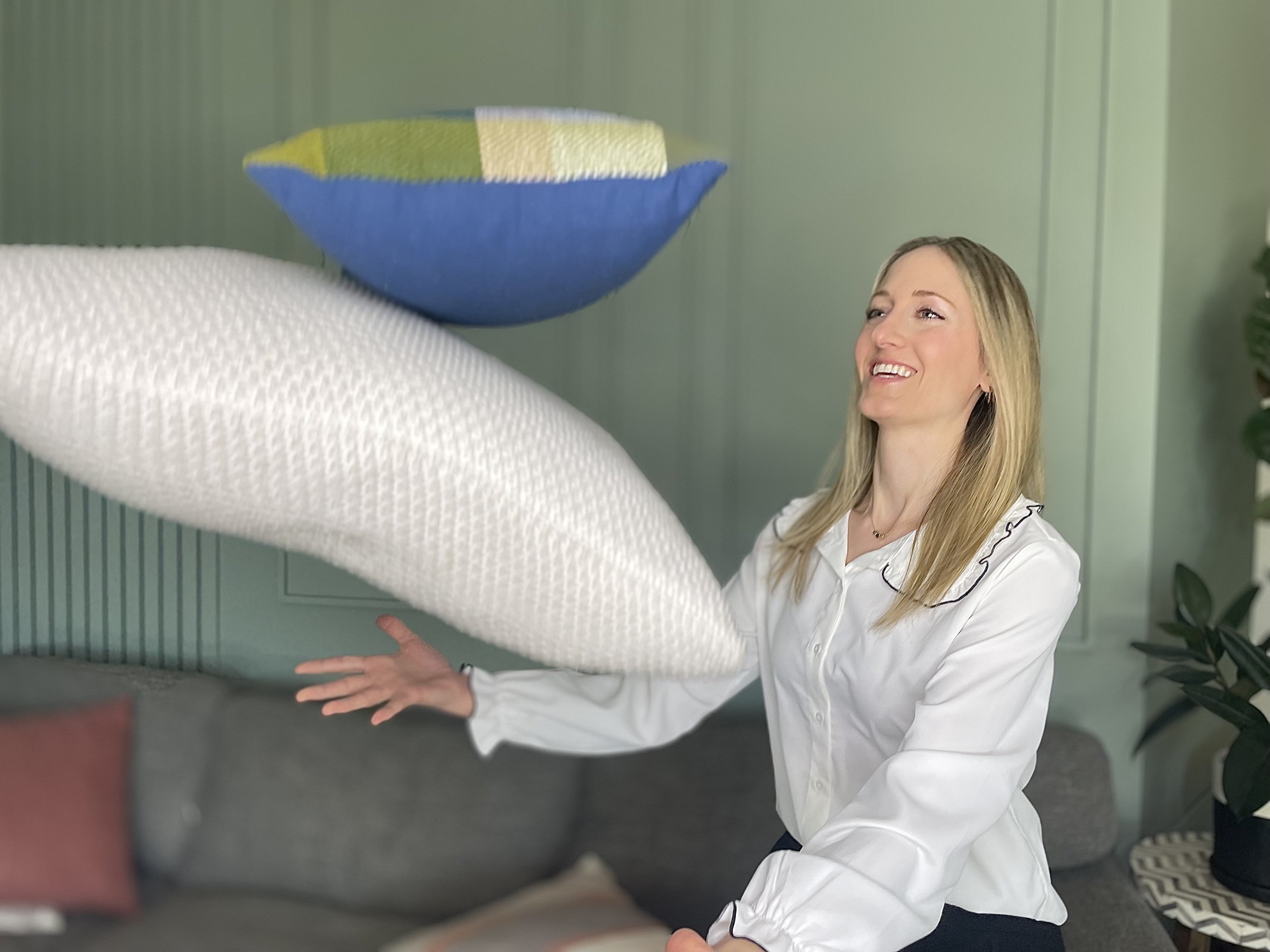 Marissa, owner of Fix My Space Marissa, tossing pillows in a living room, with a gray couch, a green wall, and a potted plant in the background.