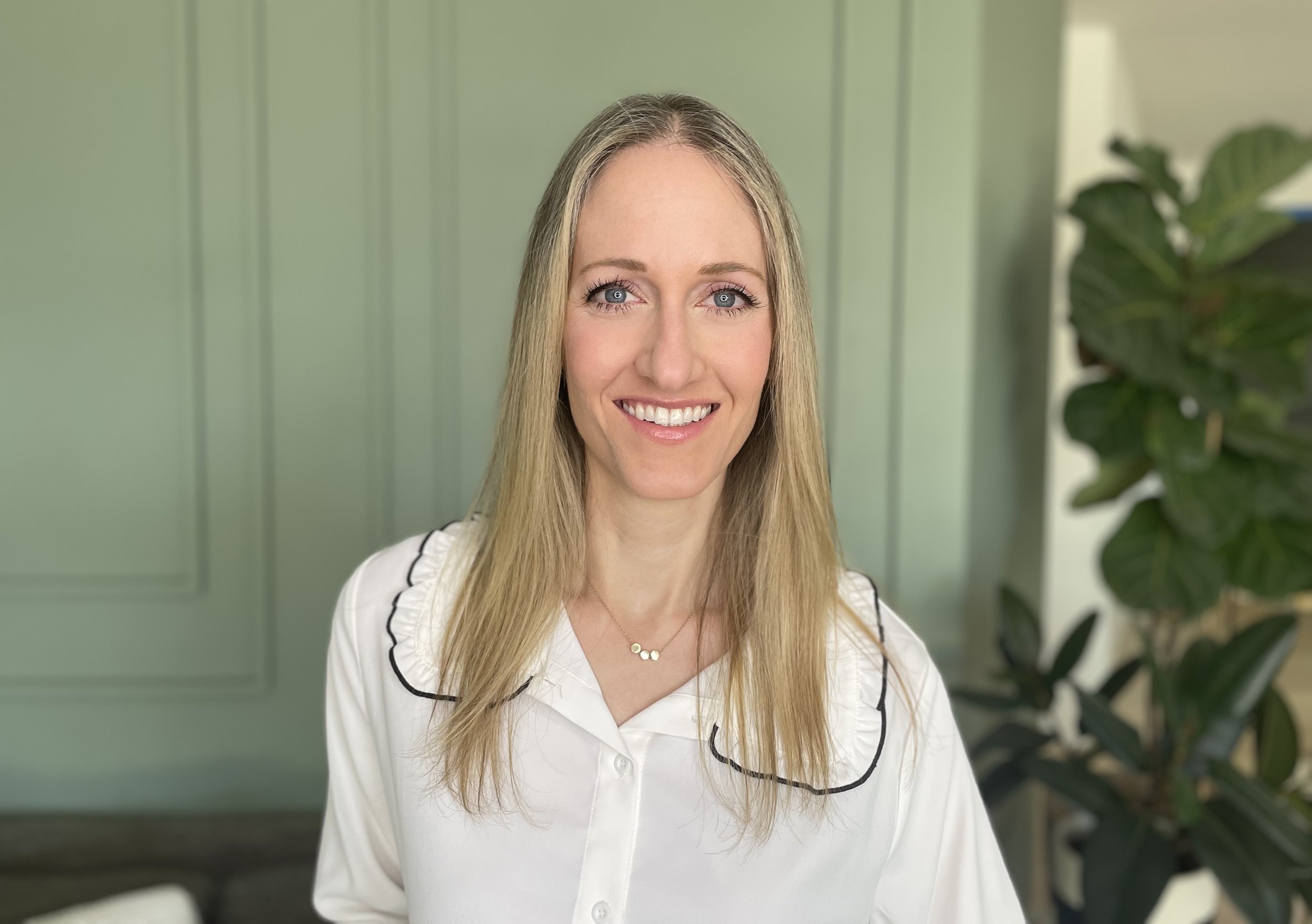 Marissa, owner of Fix My Space Marissa, smiling in front of a green wall and a large leafy plant.